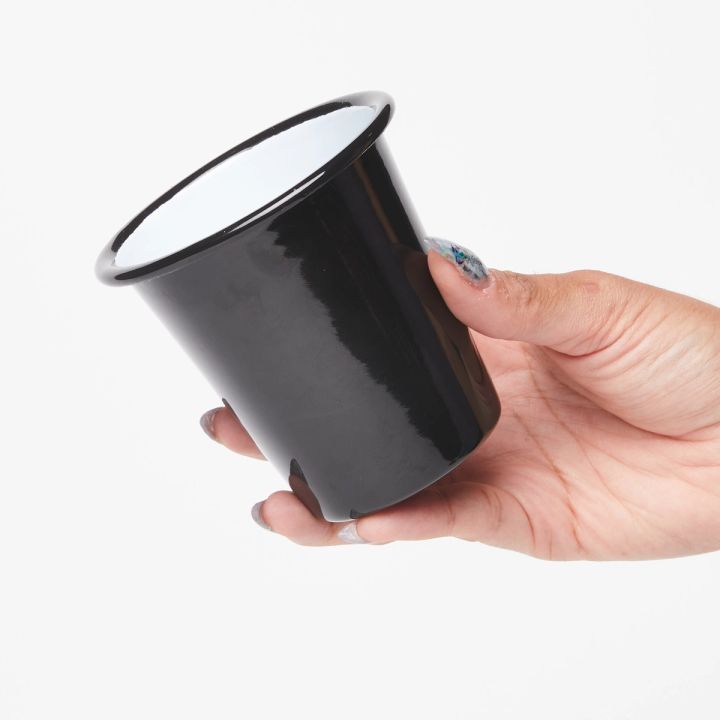 Hand holding a short enamel cup with black exterior and white interior