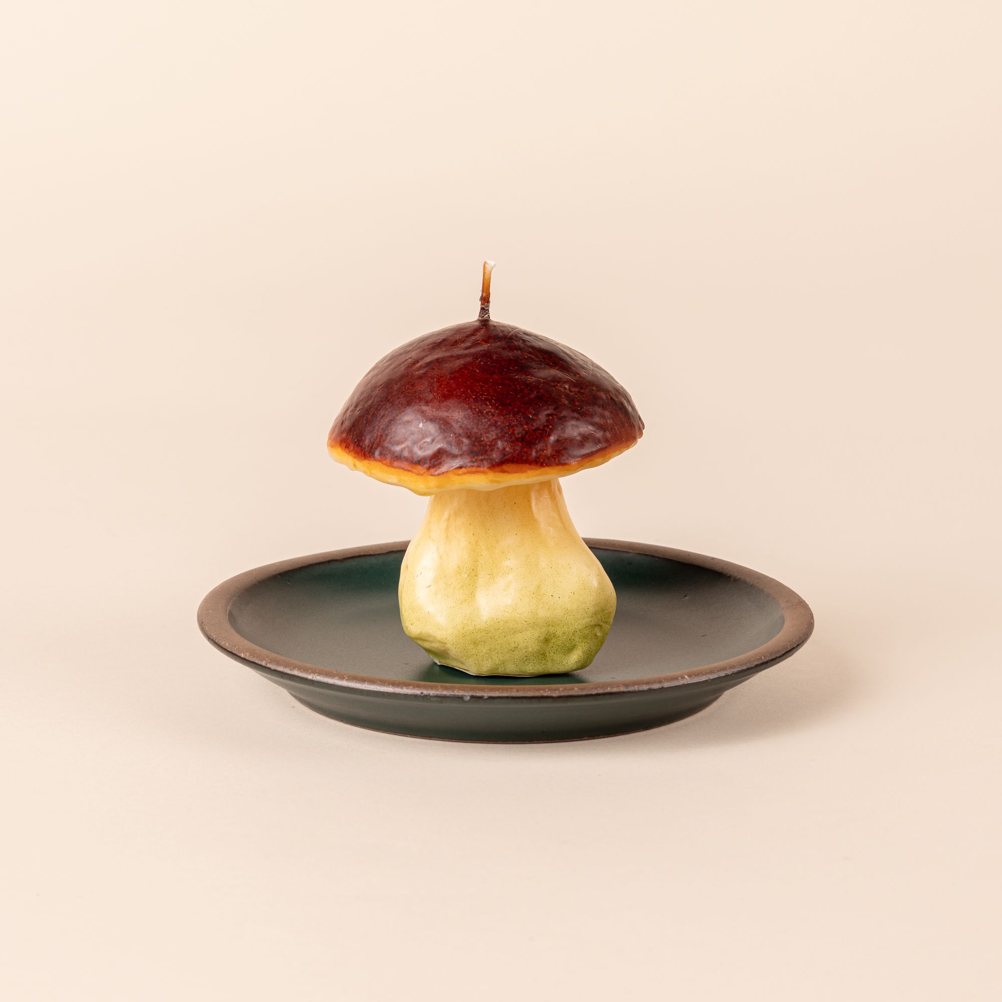 A candle that looks like a wild mushroom with a dark red top sits on a small plate.