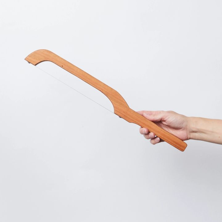Hand holding a wooden bread bow, which has a metal blade that span between curved ends of the handle