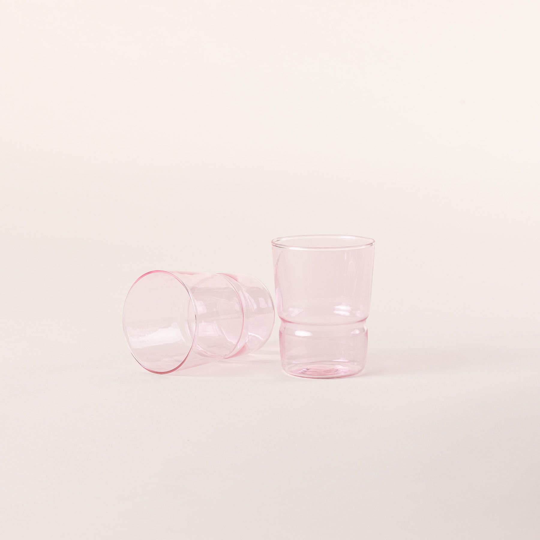 Two tumbler glasses that widens at the top in a pink color, 1 is standing up and 1 is laying on the side.