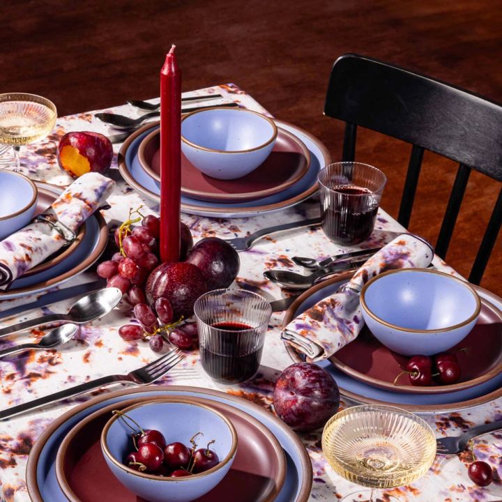 A colorful tablescape with periwinkle and plum dishes, a red taper candle, cherries, and wine glasses.