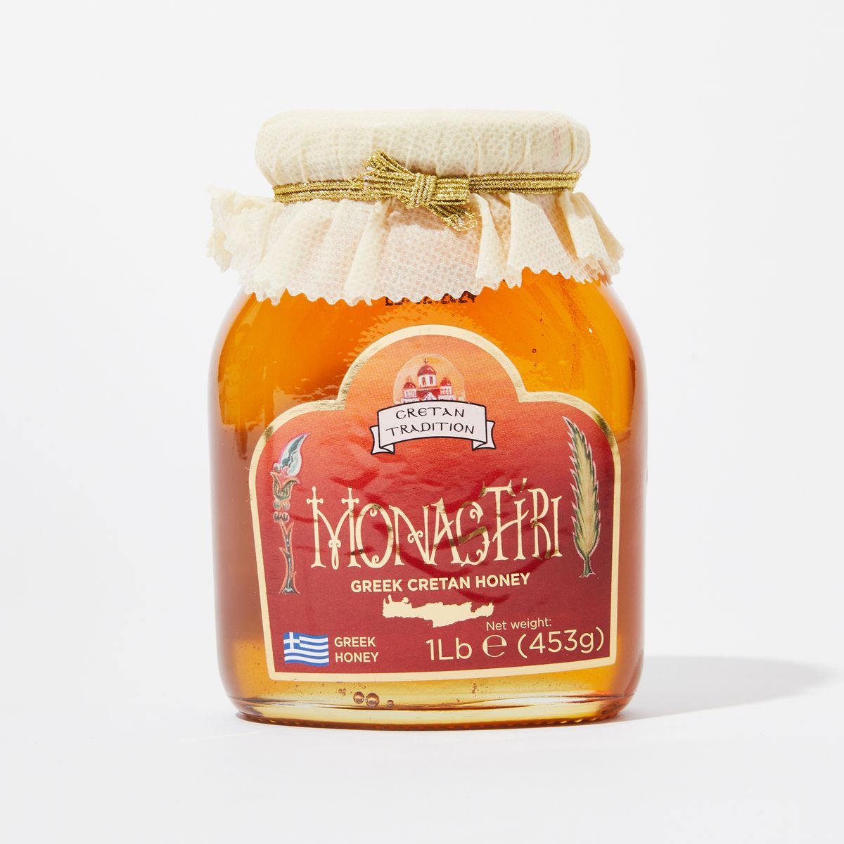 A clear jar full of golden honey with fabric tied around the lid and a red label that reads "Monastiri Greek Cretan Honey"