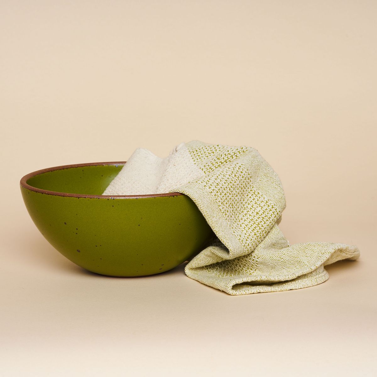 A mossy-green pottery bowl with a matching green-and-natural fiber handwoven tea cloth whimsically placed within it