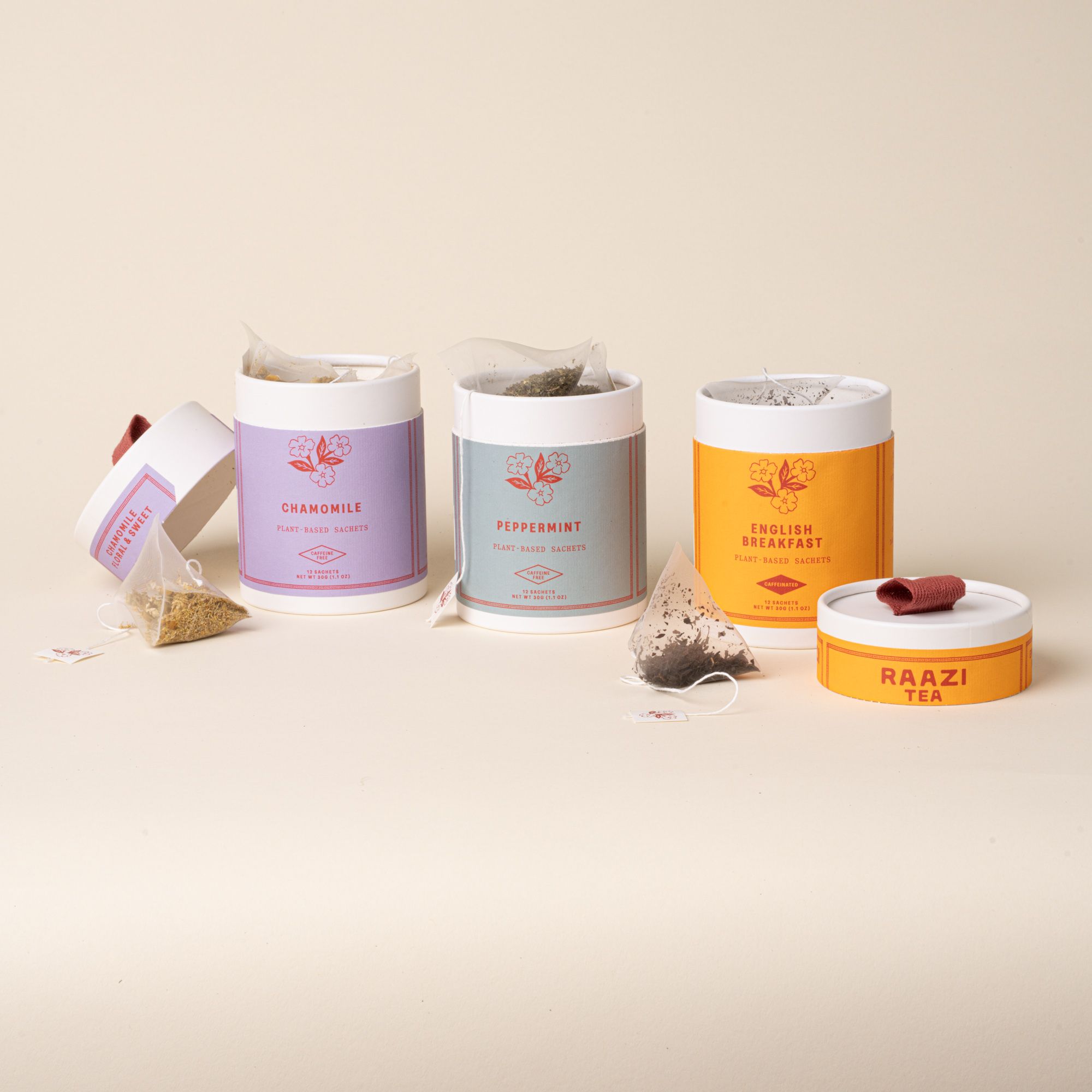 Three open RAAZI Tea tins (chamomile, peppermint, English breakfast) with loose sachets and lids on a neutral background.