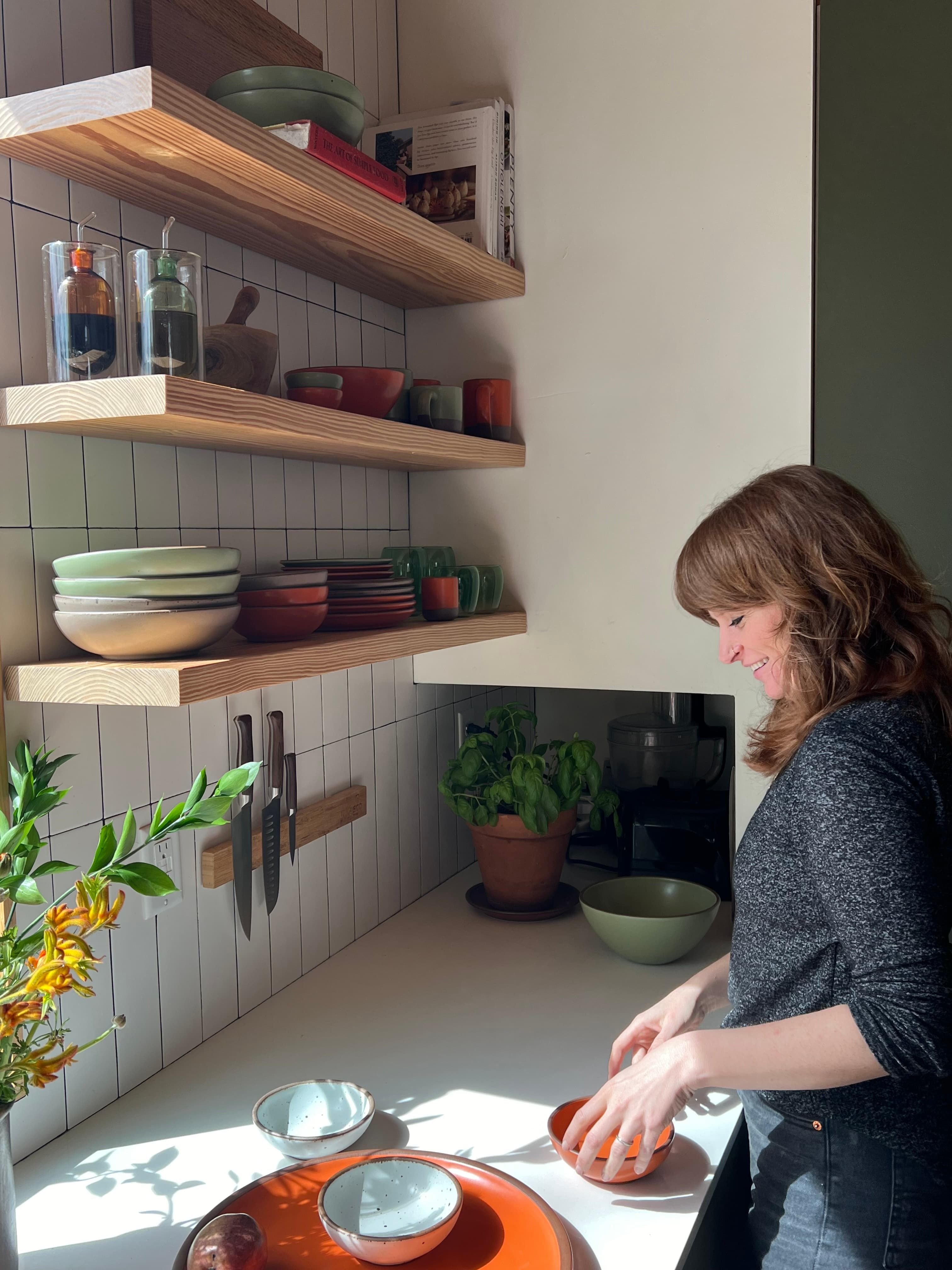 Nicole is arranging ceramic bowls in a bold orange color in a kitchen.