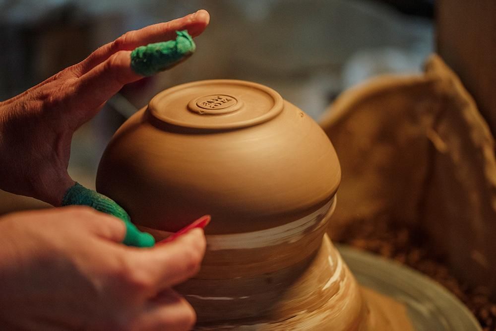 Hands trimming edges of pottery bowl