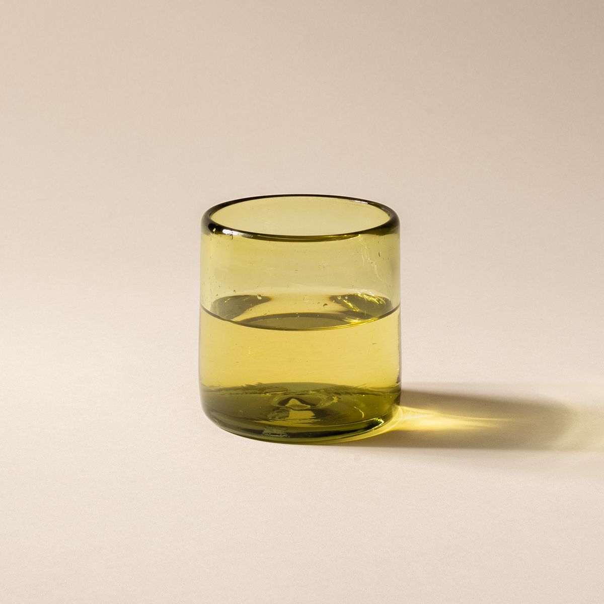 An olive green short transparent drinking glass, filled with water.