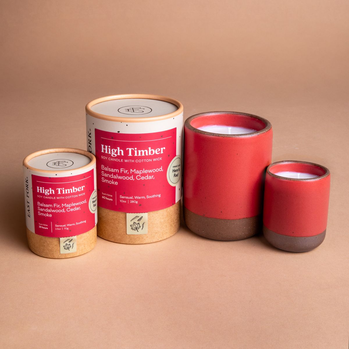 Small and large ceramic vessel next to each other in bold red color with candles inside each. Cardboard tube packaging is on the left with branding stickers that say "High Timber".