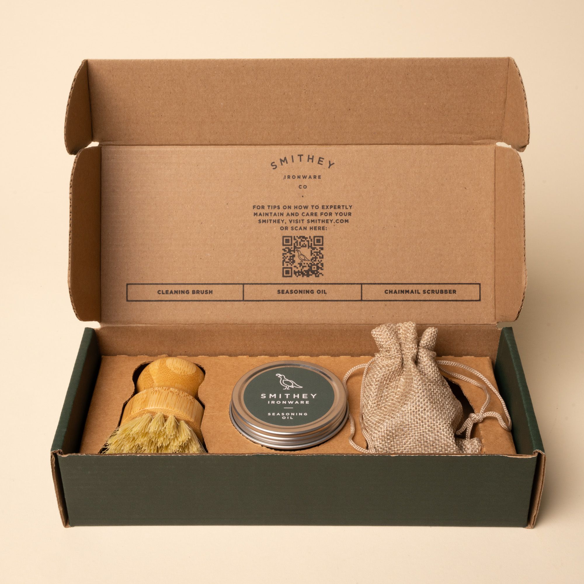 Open Smithey Ironware care kit box with cleaning brush, seasoning oil, and chainmail scrubber.