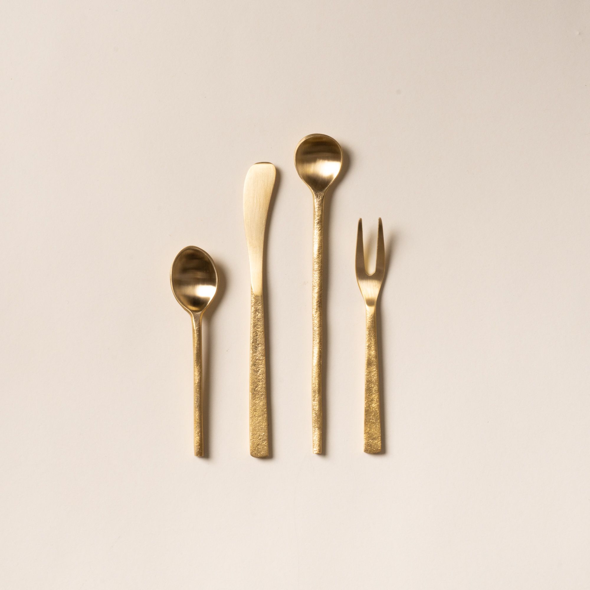 Four brass flatware utensils arranged on a light background
