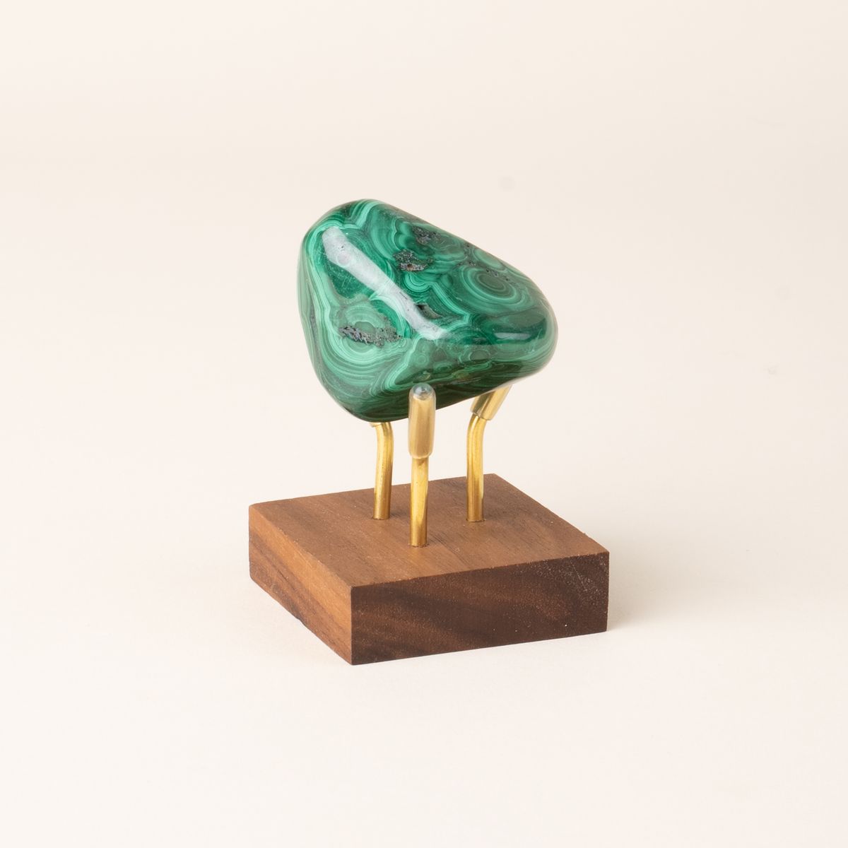 A polished green malachite stone with swirling banded patterns is displayed on a small wooden base with three gold metal prongs.