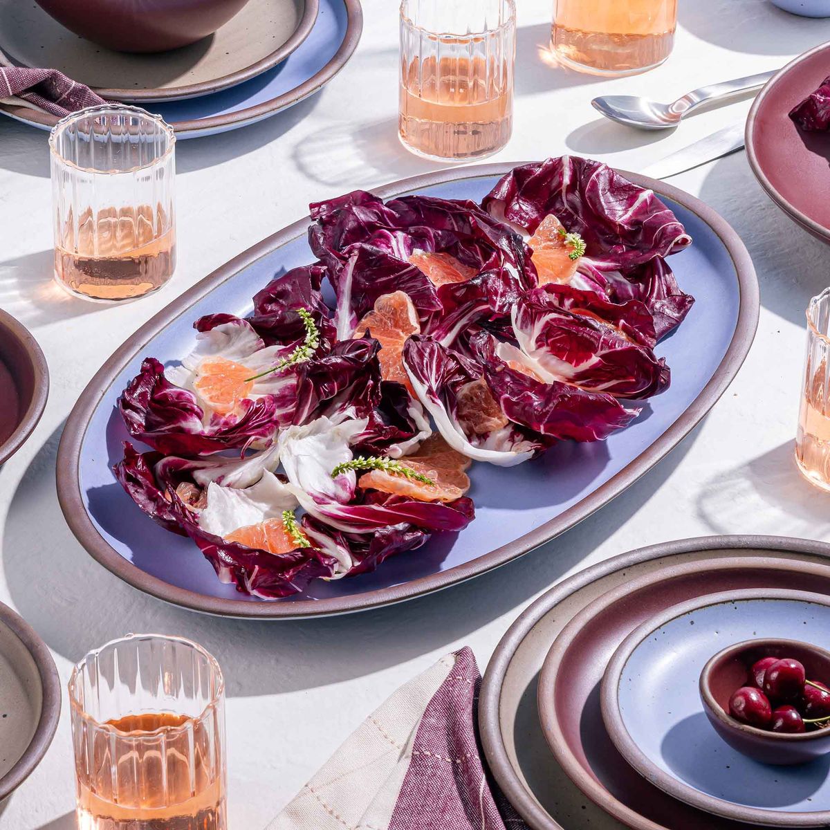 A large oval ceramic platter in a periwinkle color with a salad, surrounded by drinks.