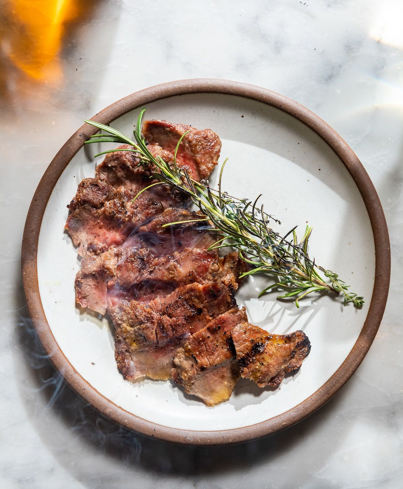 Thin sliced steak plated on East Fork Eggshell plate with rosemary and smoke