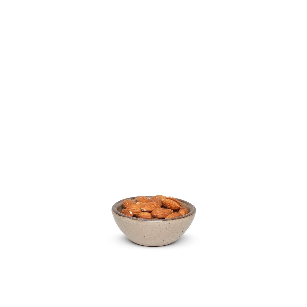 A tiny rounded ceramic bowl in a warm pale brown color featuring iron speckles and an unglazed rim, filled with almonds