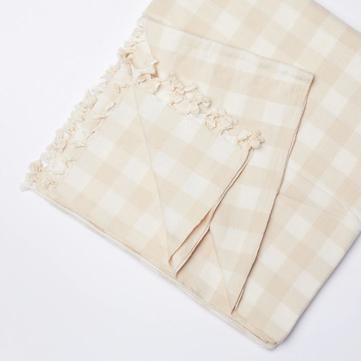 A folded cream and white gingham cotton tablecloth with one corner pulled back