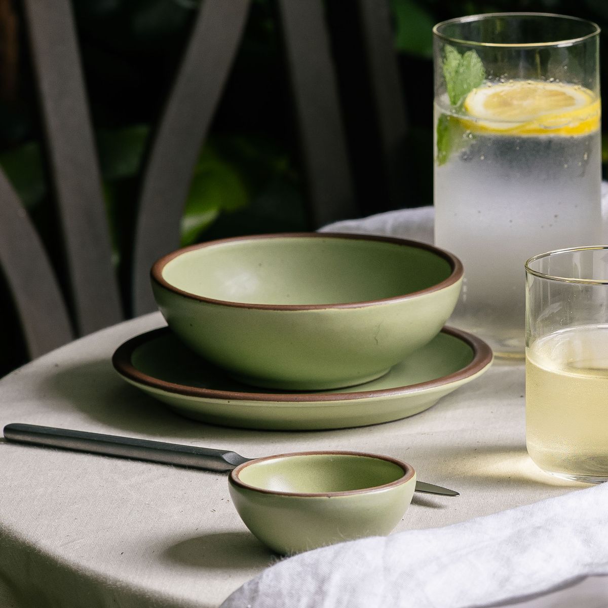 A shallow sage green bowl on a dessert-sized plate surrounded by a glass of water and a small glass of white wine.