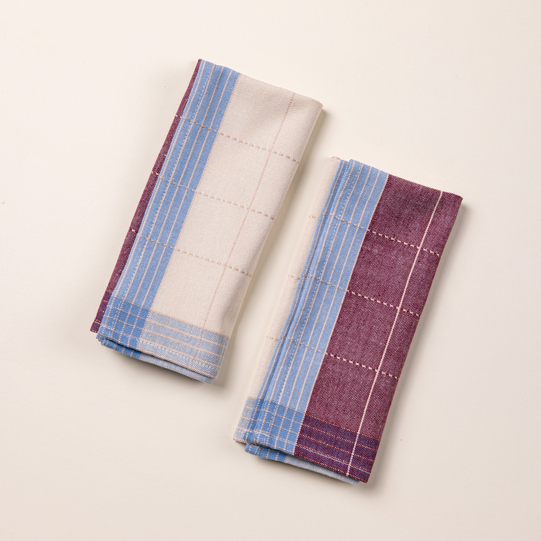  Two folded plum and periwinkle colored napkins side by side. They have a plaid design with white grid lines.