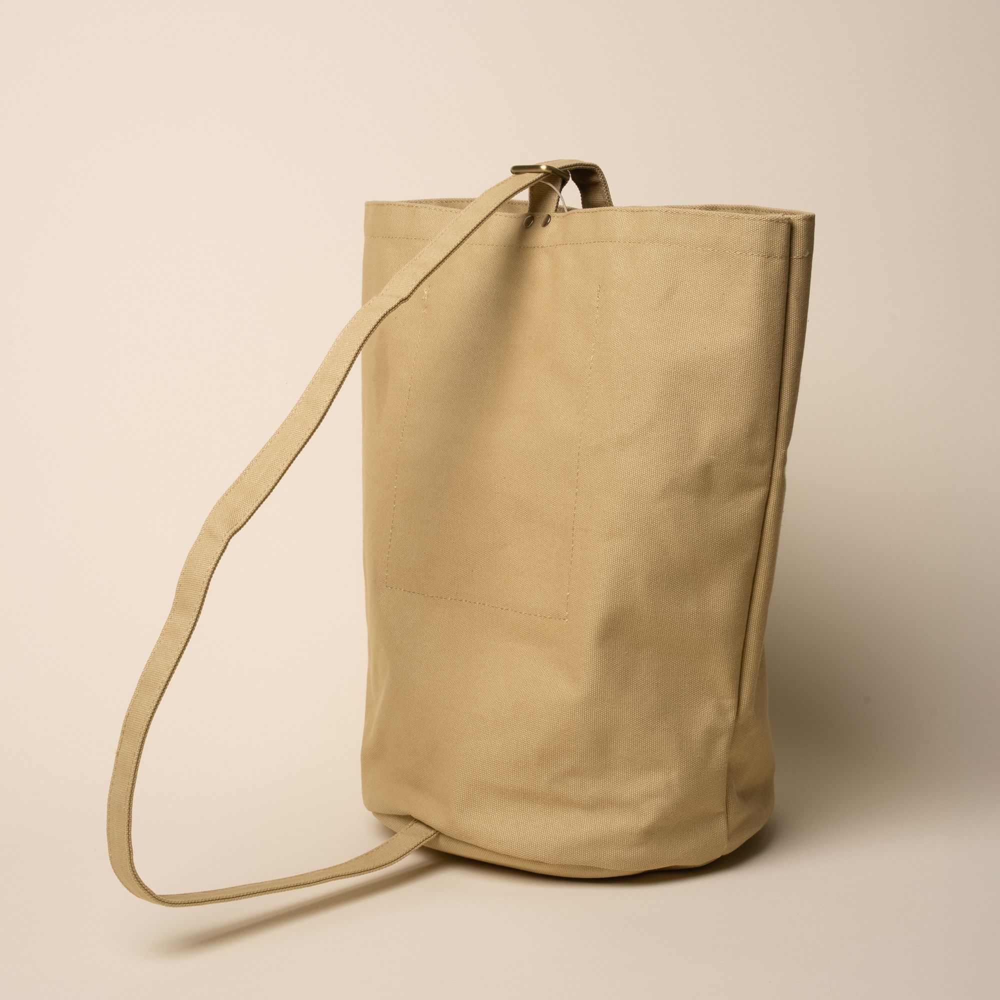The back of a large simple canvas bucket tote with a strap to hang over your shoulder