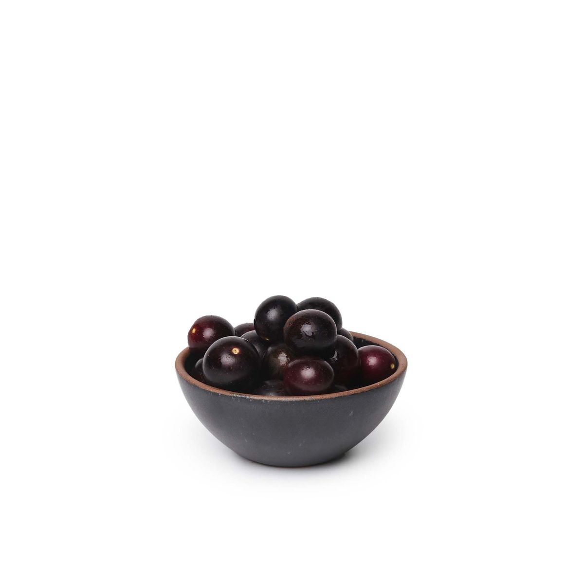 A small dessert sized rounded ceramic bowl in a graphite black color featuring iron speckles and an unglazed rim, filled with cherries