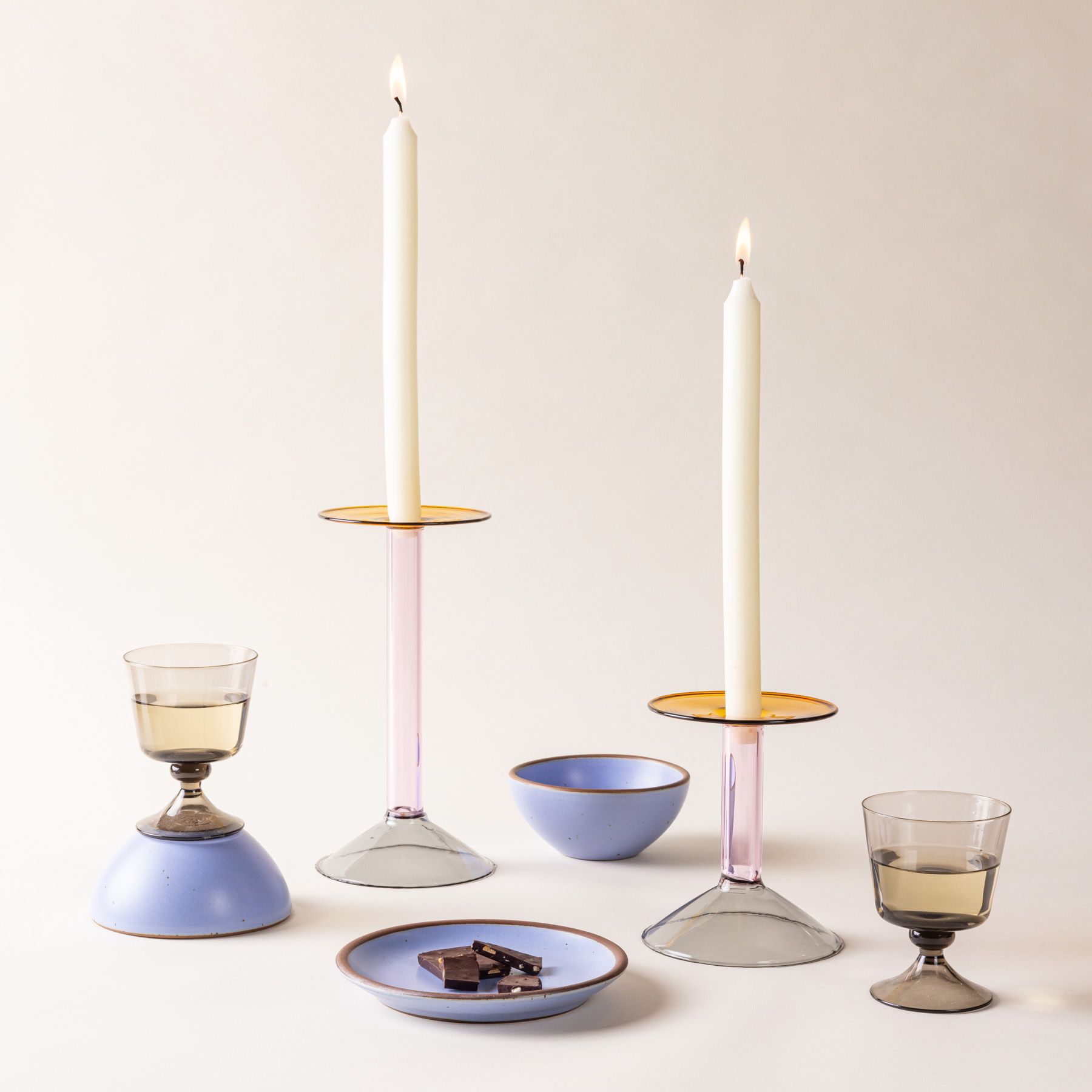 Two modern angular glass candle holder with cream taper candles, periwinkle bowls and plates, and wine glasses