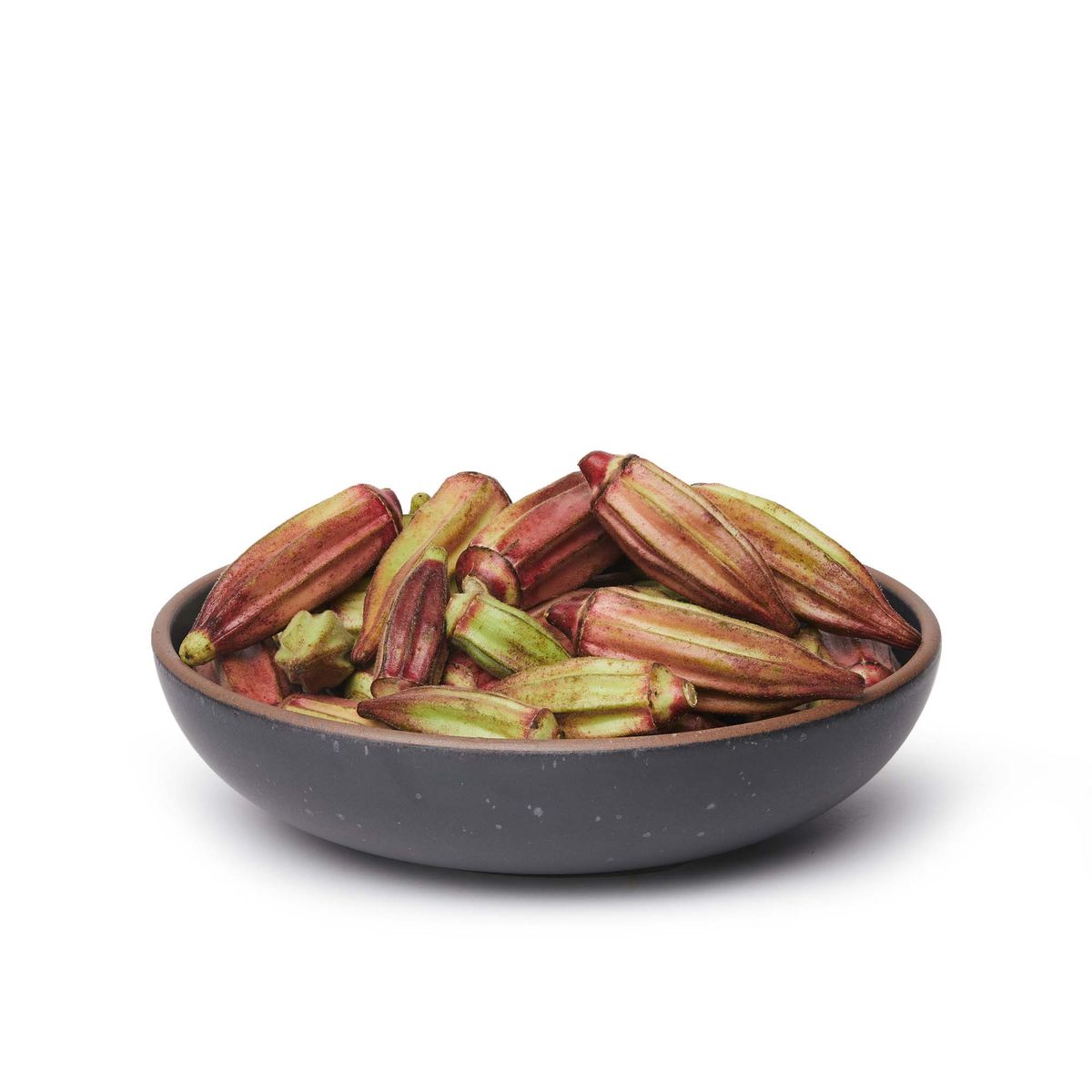 A large shallow serving ceramic bowl in a graphite black color featuring iron speckles and an unglazed rim, filled with okra