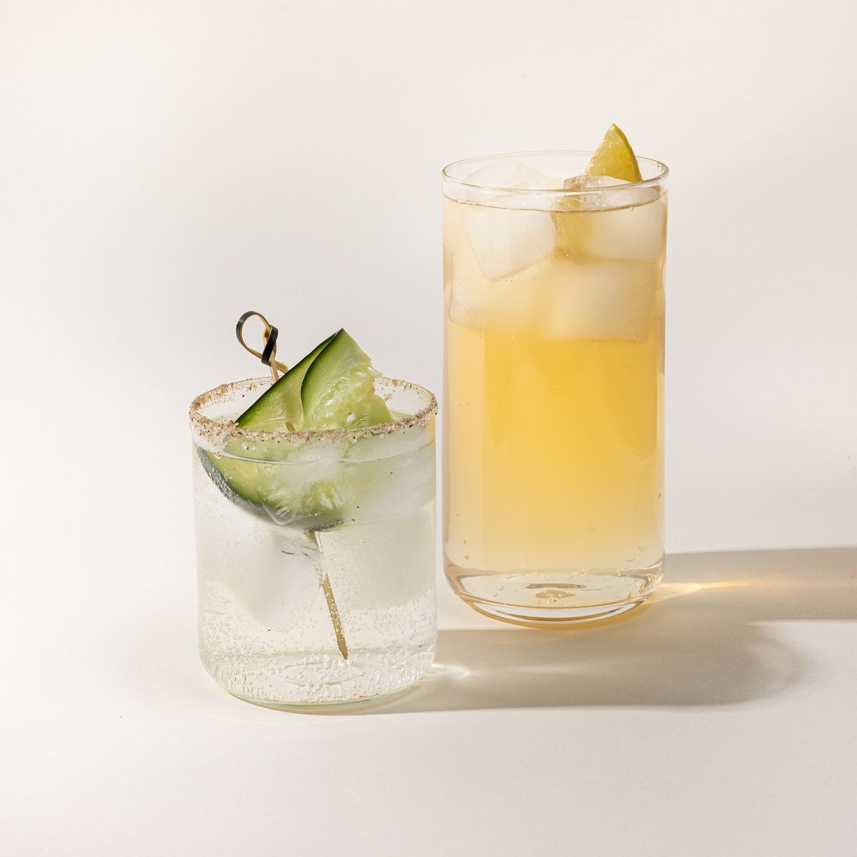 A straight walled tall and short glass cup with cocktails inside and fruit garnish.