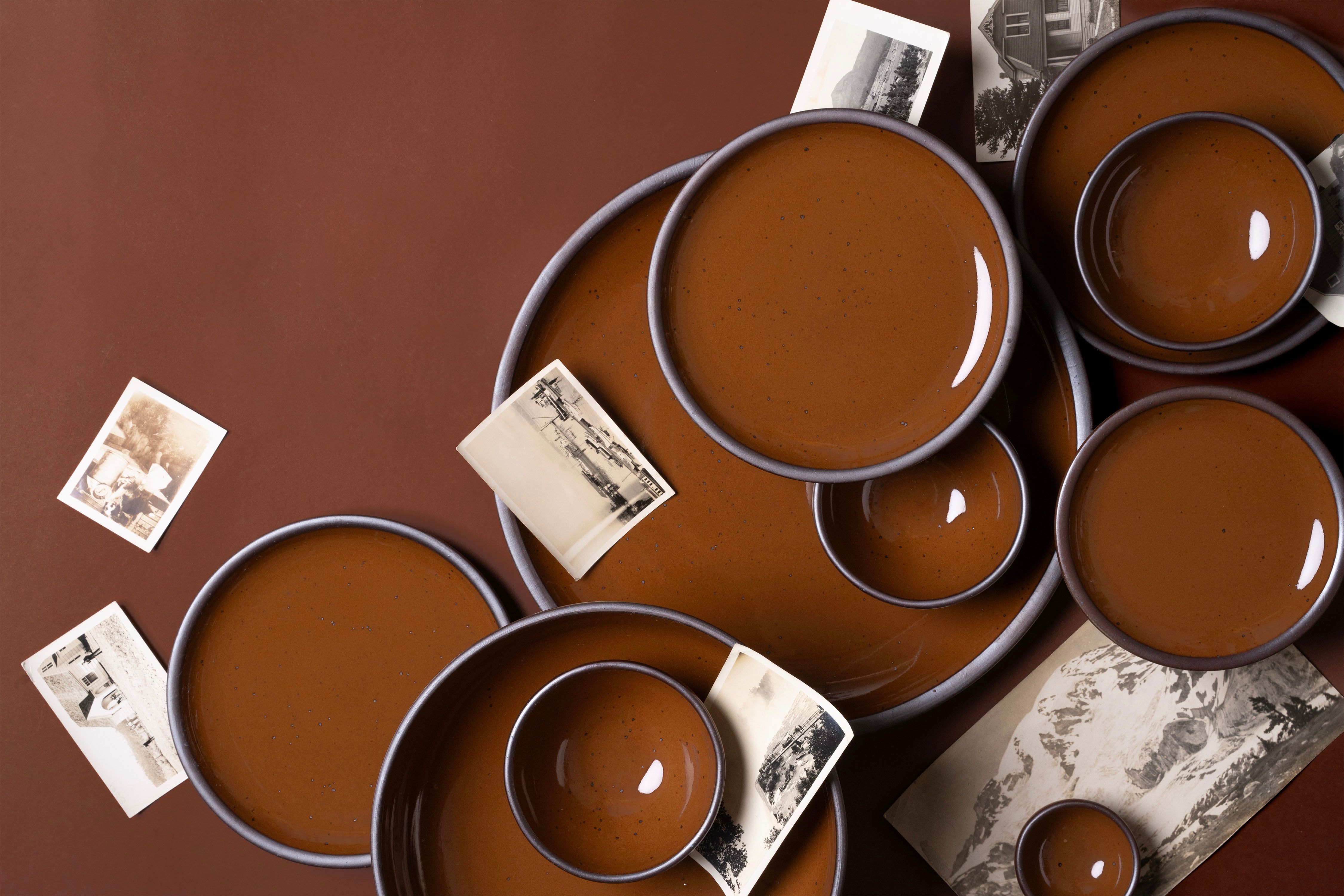 Arrangement of glossy caramel brown ceramic plates and bowls with scattered vintage black-and-white photographs.
