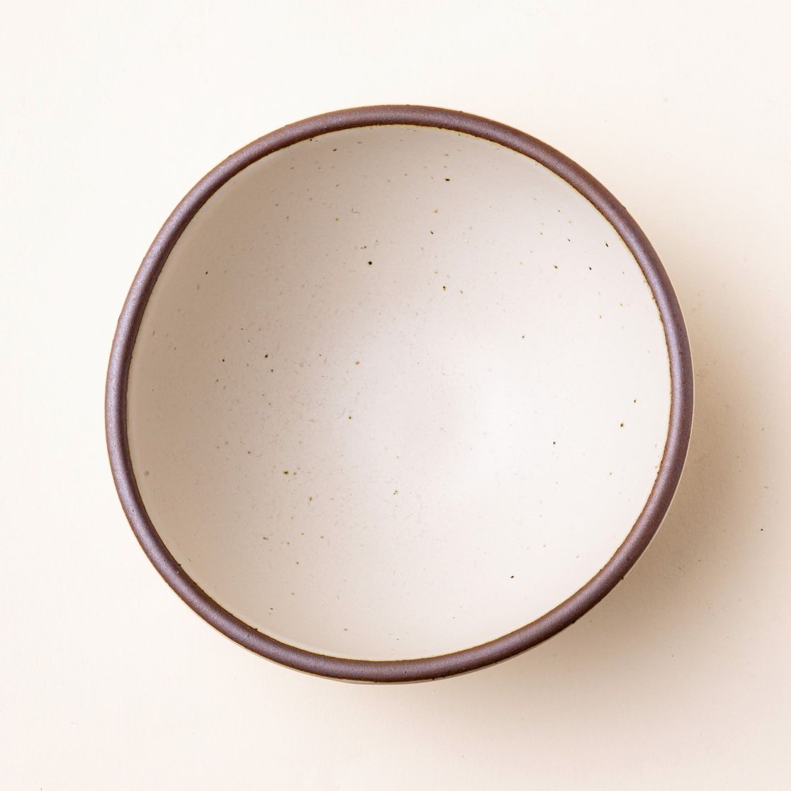 Overhead view of a ceramic bowl in an off-white color with warping.