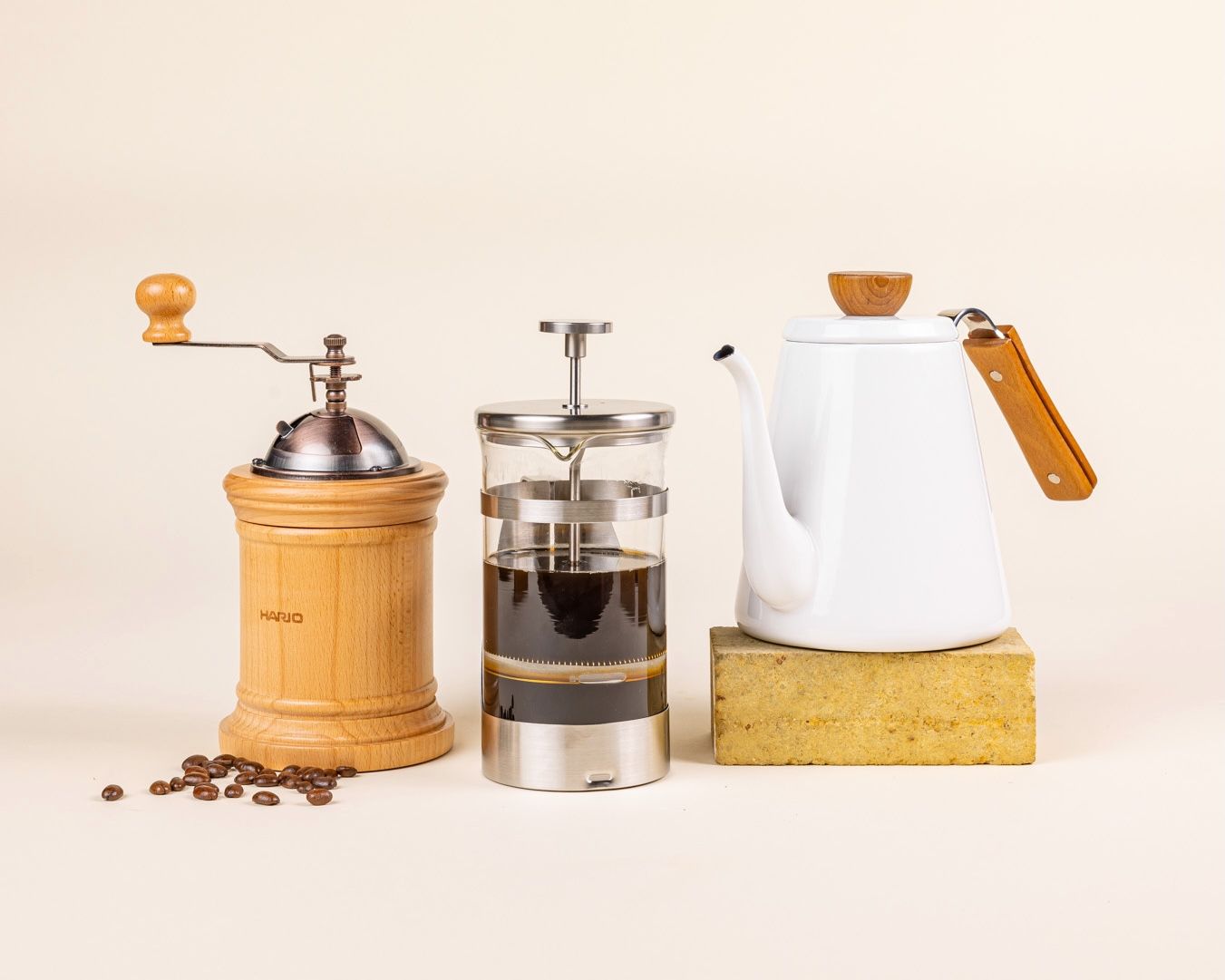 3 coffee accessories including a coffee grinder, a french press, and a white tea kettle.