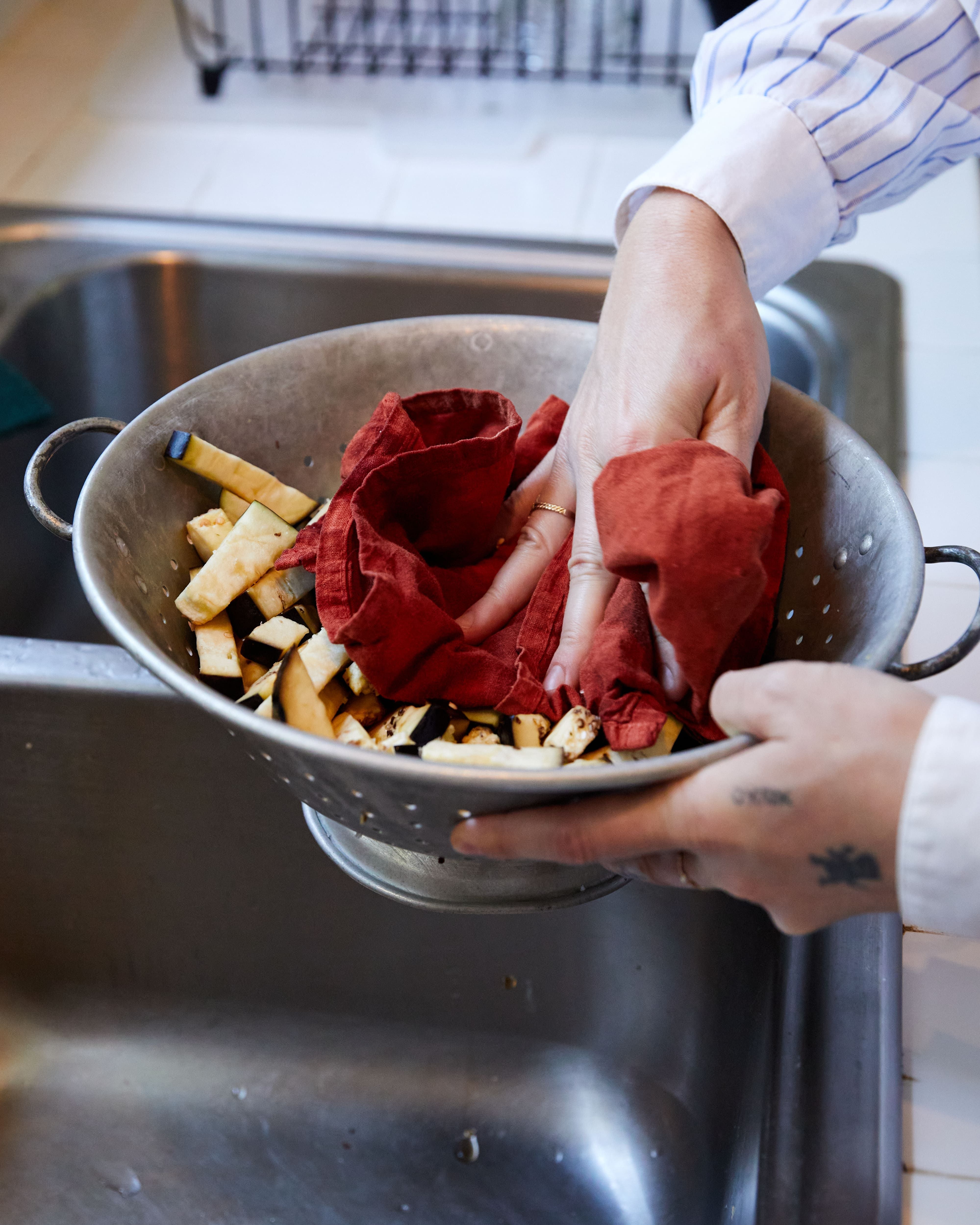 Hands hold a metal strainer cleaning sliced eggplant strips