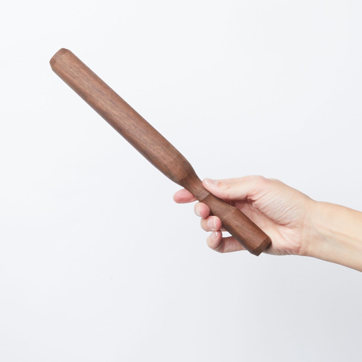 Hand holding a long walnut wood cocktail muddler that tapers slightly towards the handle