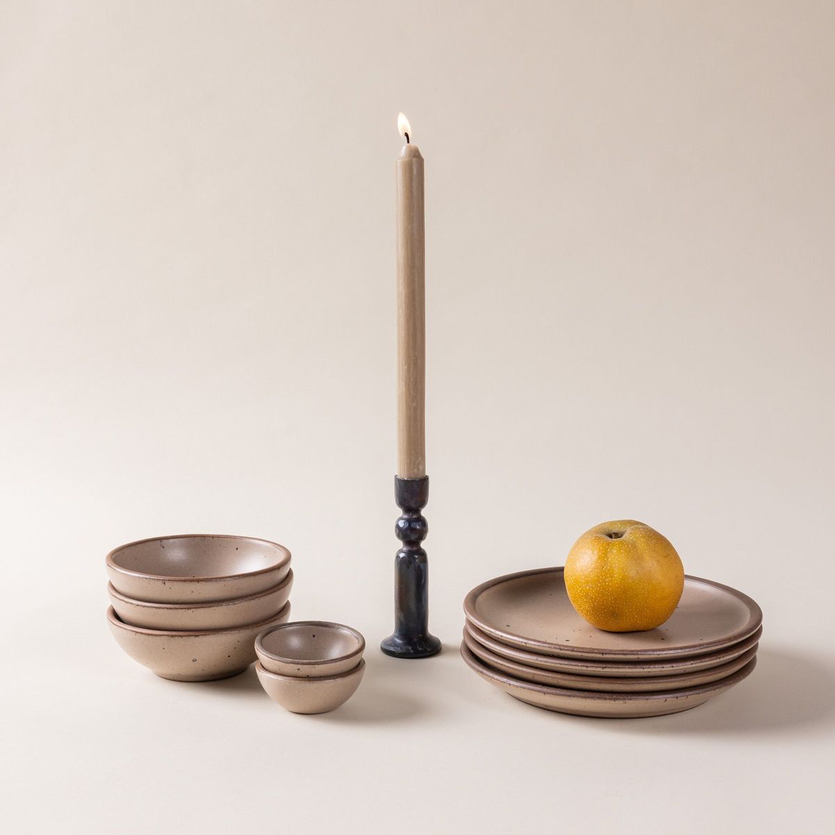 A beige taper candle in an iron candleholder with warm tan bowls and plates.