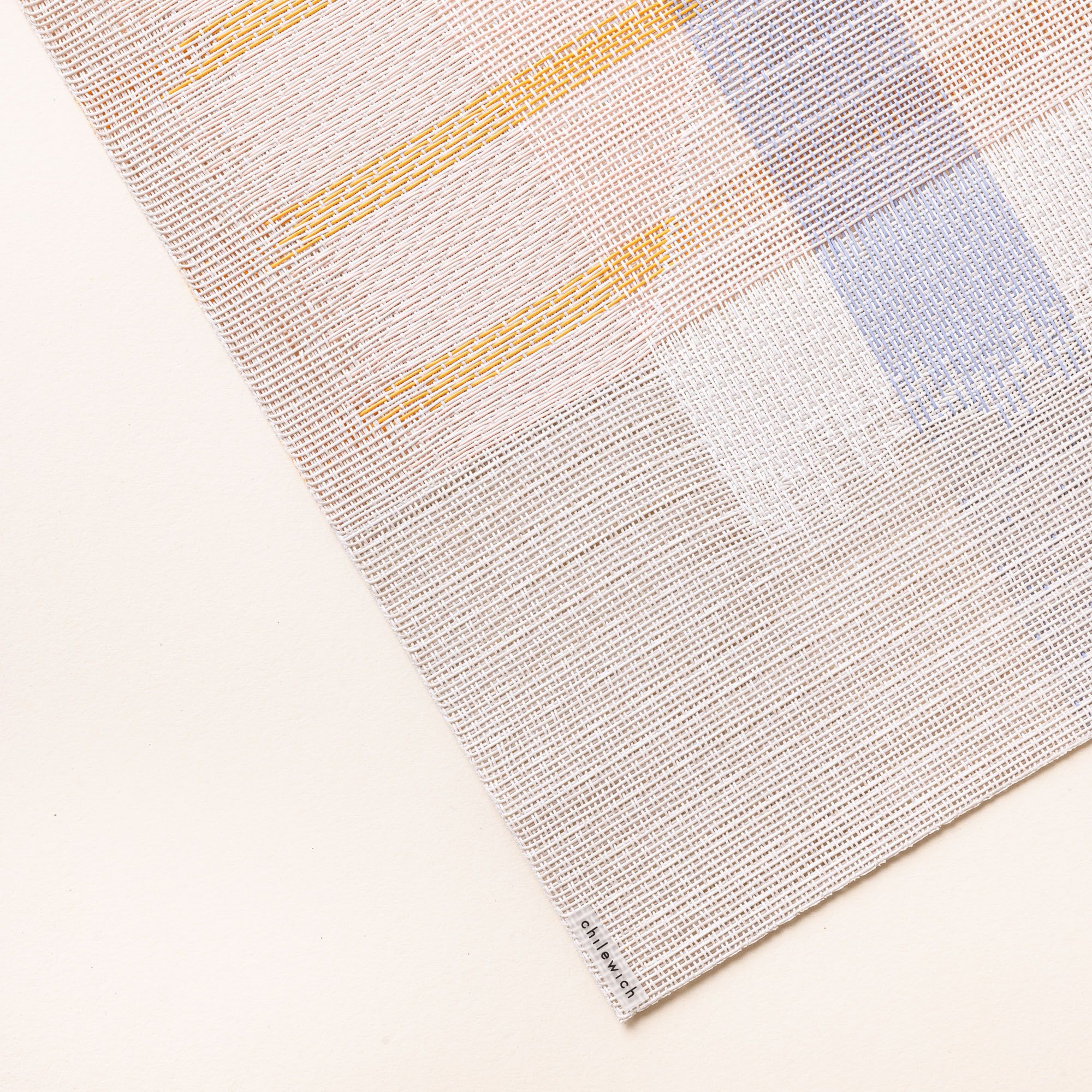 A close up of a corner of a placemat with a soft artful geometric design featuring neutral, orange, white, and blue colors
