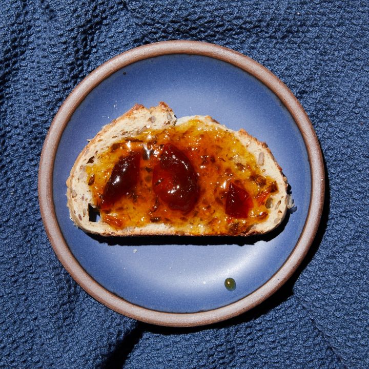 Amber jam spread on bread on a blue side plate on top of blue waffle towel