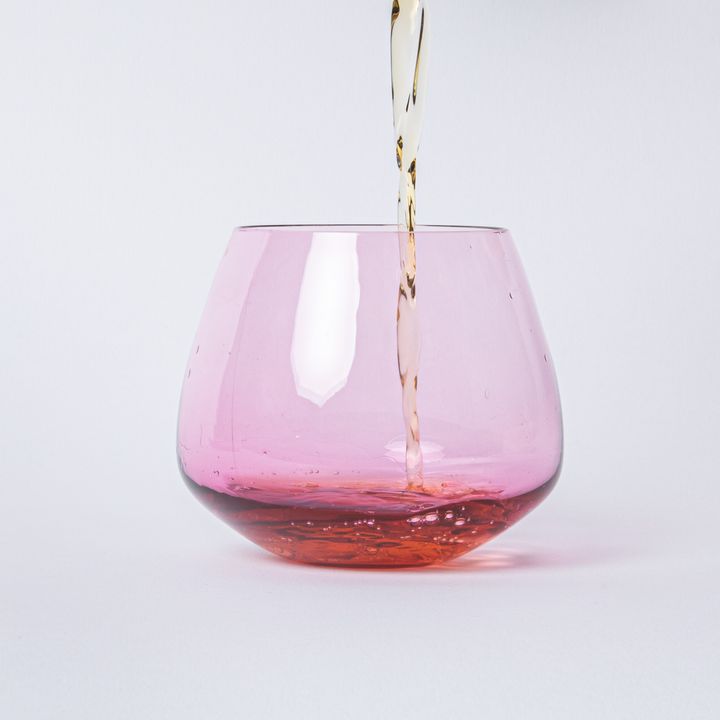 A drink being poured into a clear pink glass whiskey snifter with a rounded base
