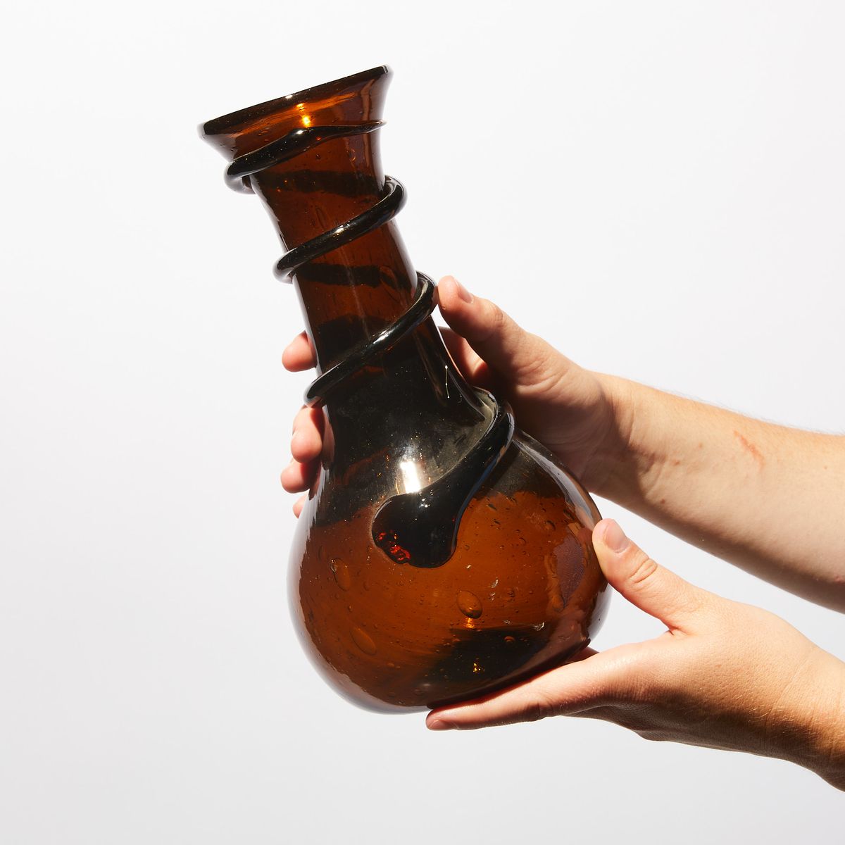 Hand holding Translucent Brown glass vase with black swirl going up the neck