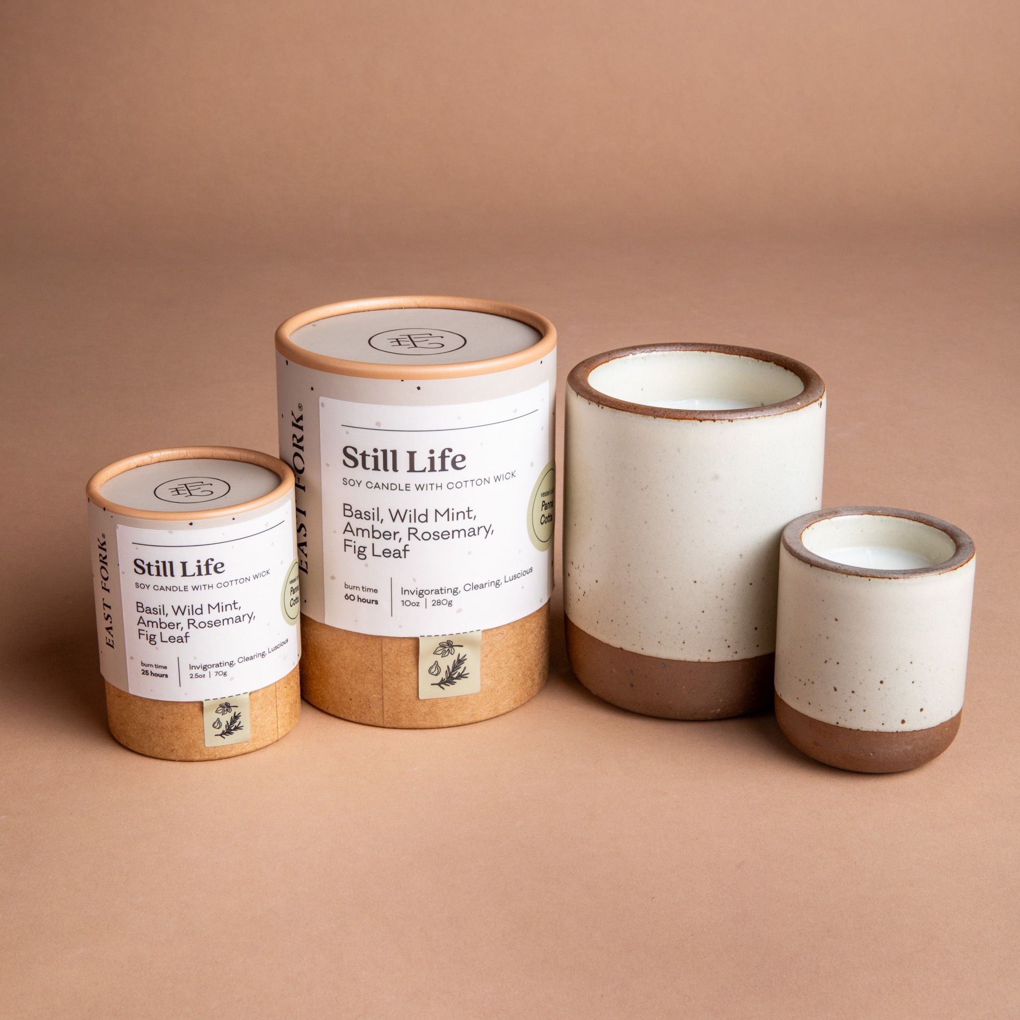 Small and large ceramic vessel next to each other in a warm off-white color with candles inside each. Cardboard tube packaging is on the left with branding stickers that say "Still Life".