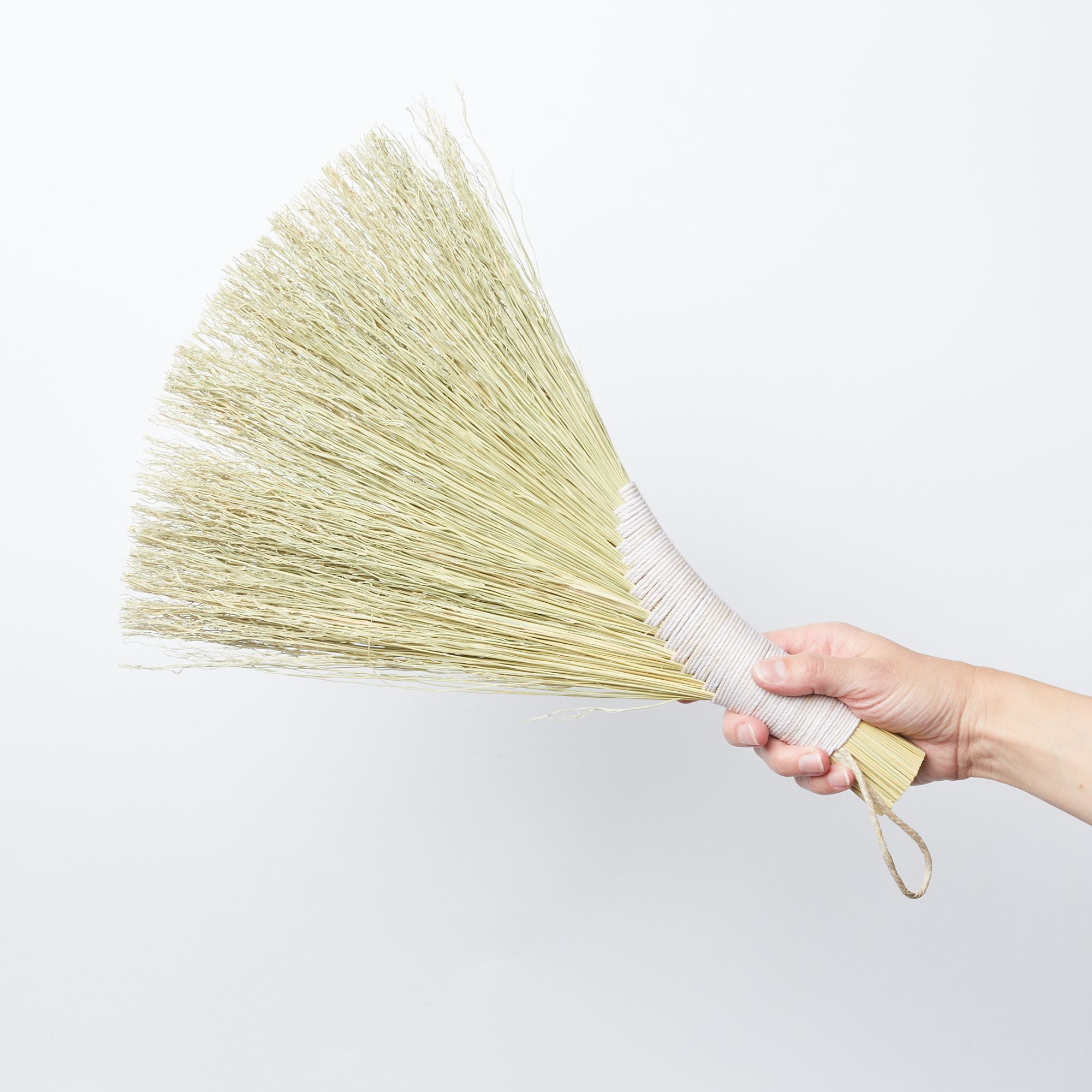 Hand holding a broom of sorghum that is tied at the handle and fans out at the head