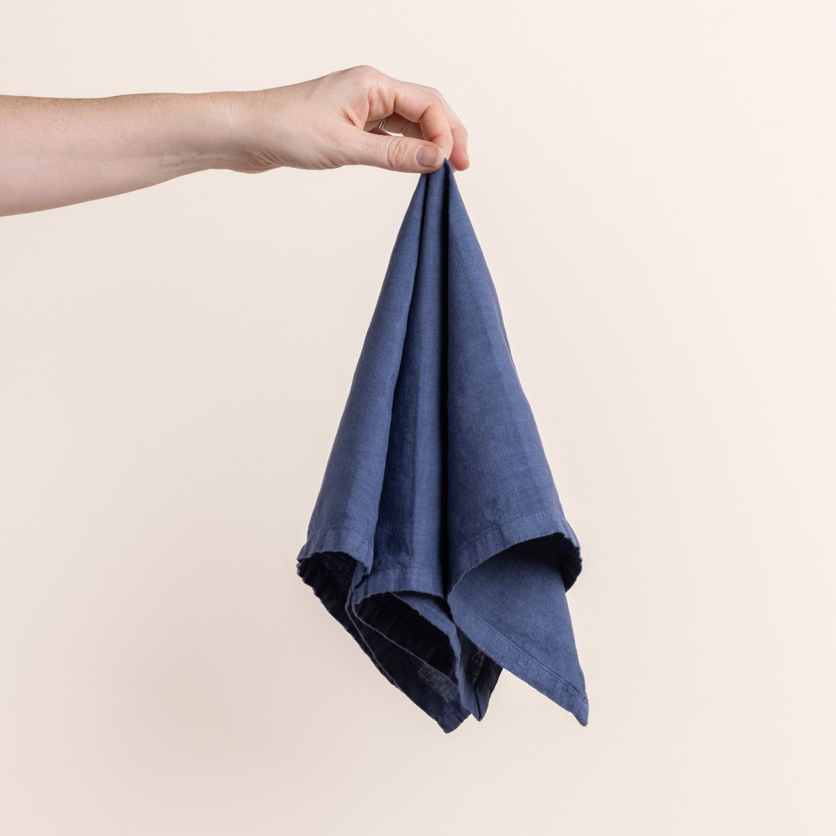 Hand holding a linen napkin in a muted blue color from the center 