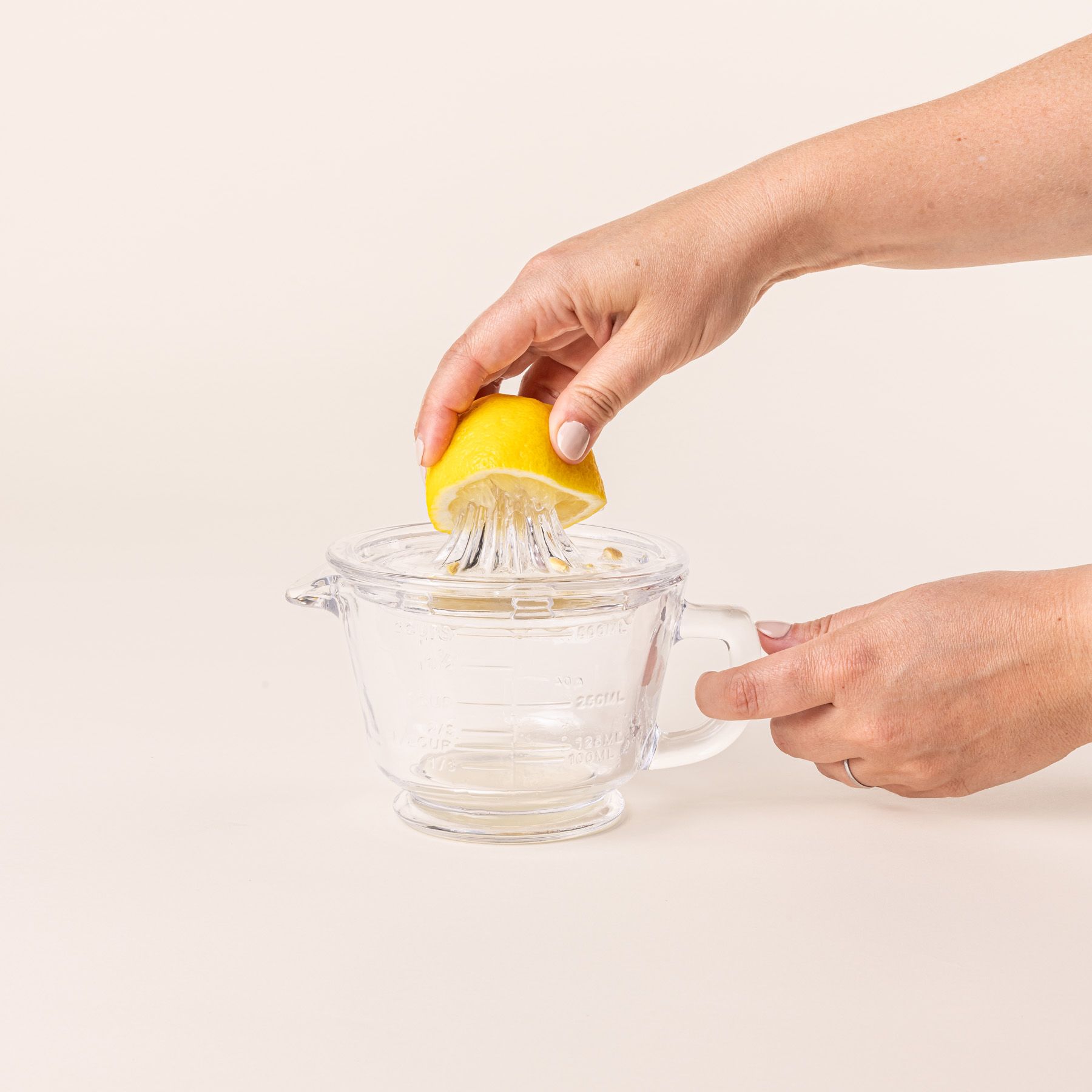 A hand juices a lemon on a traditional glass juicer with a handle and removable top