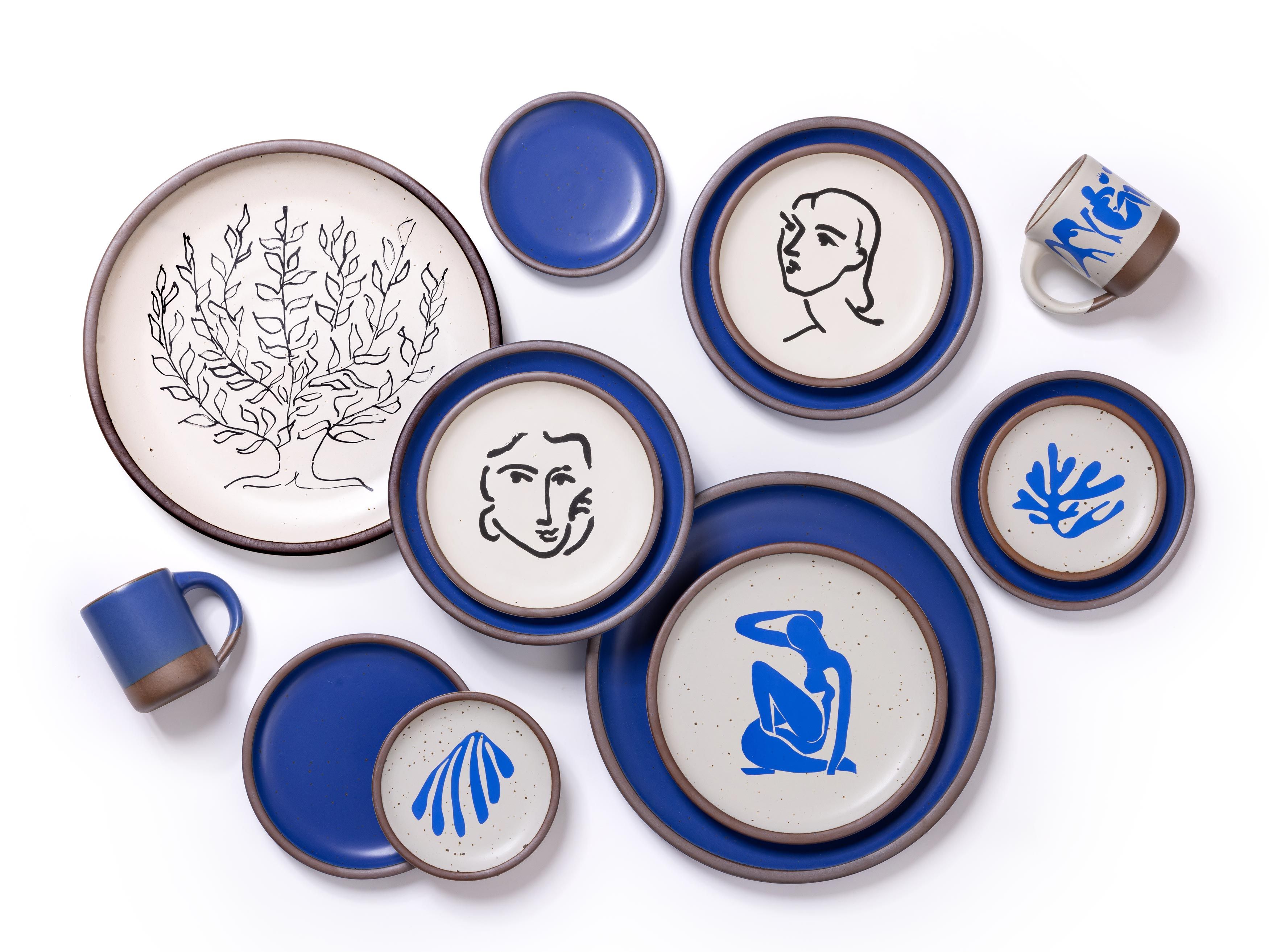 Ceramic plates and mugs with decals of Henri Matisse's artworks along with a cobalt blue plates and mugs on white background.
