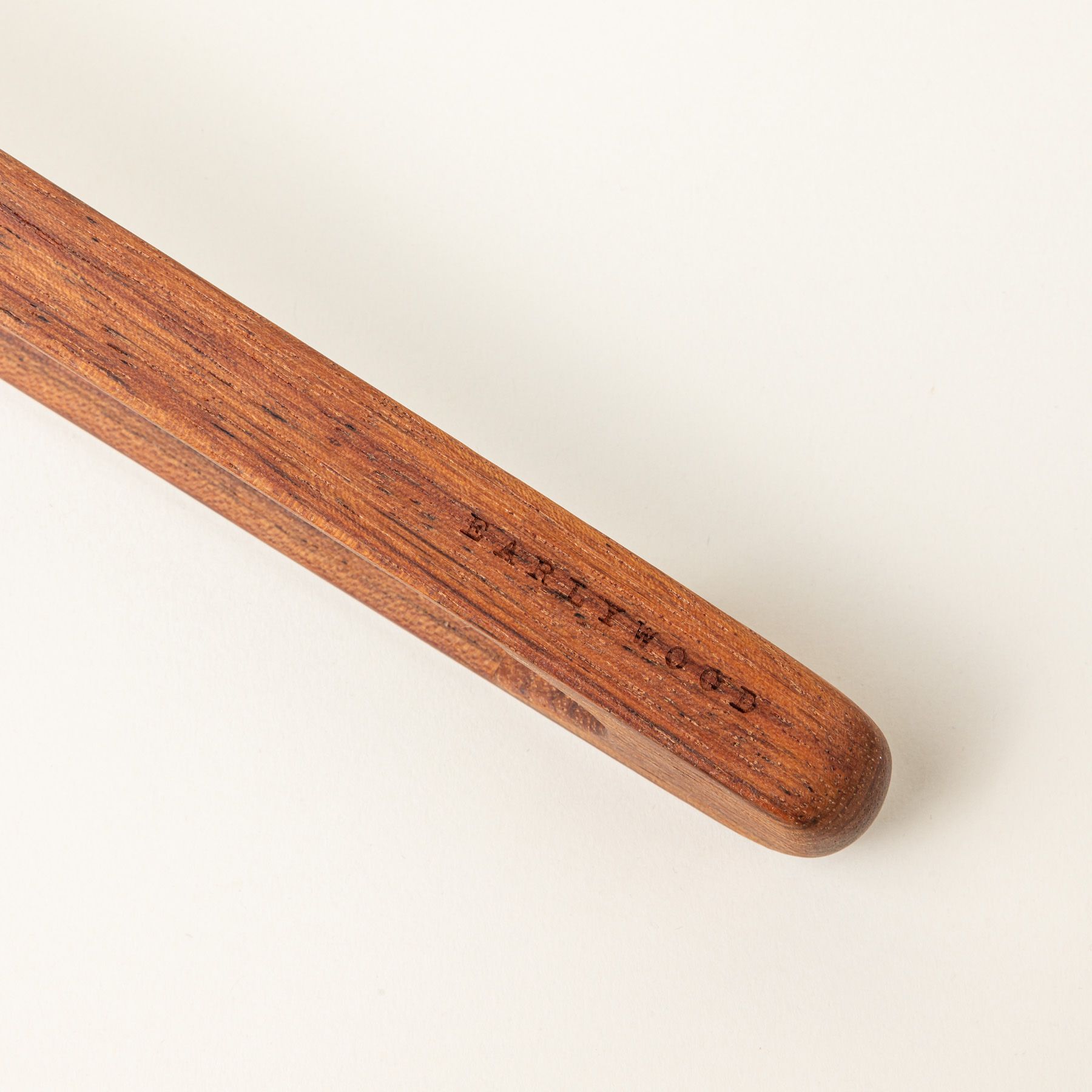 A close up of the end of a simple and minimal wood rectangular tongs, one side reads 'Earlywood'