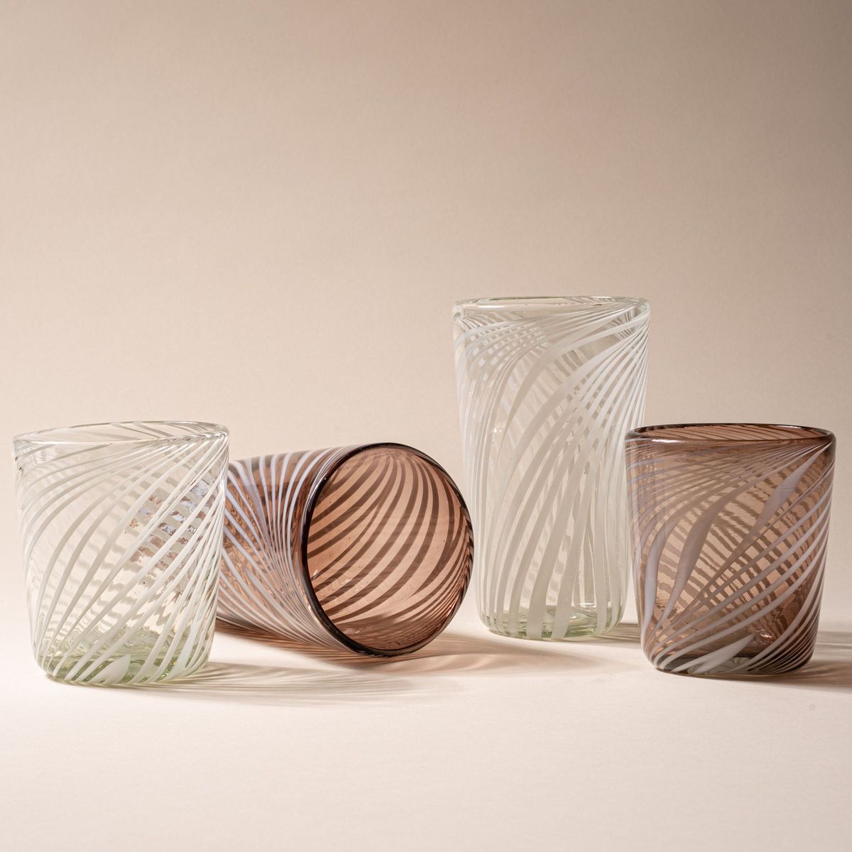 Set of clear and smoky glass tumblers with white swirl patterns, arranged upright and on their side.
