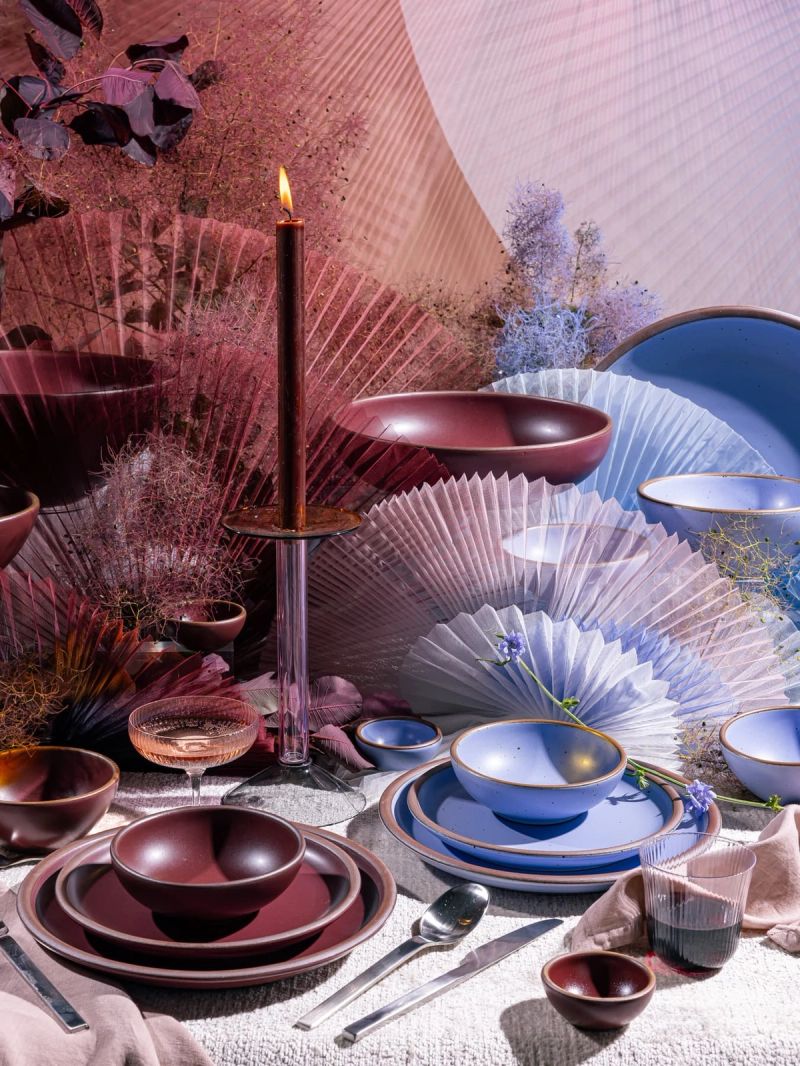A beautiful tablescape filled with artful fabric sculptures, and ceramic plates and bowls in periwinkle and plum colors