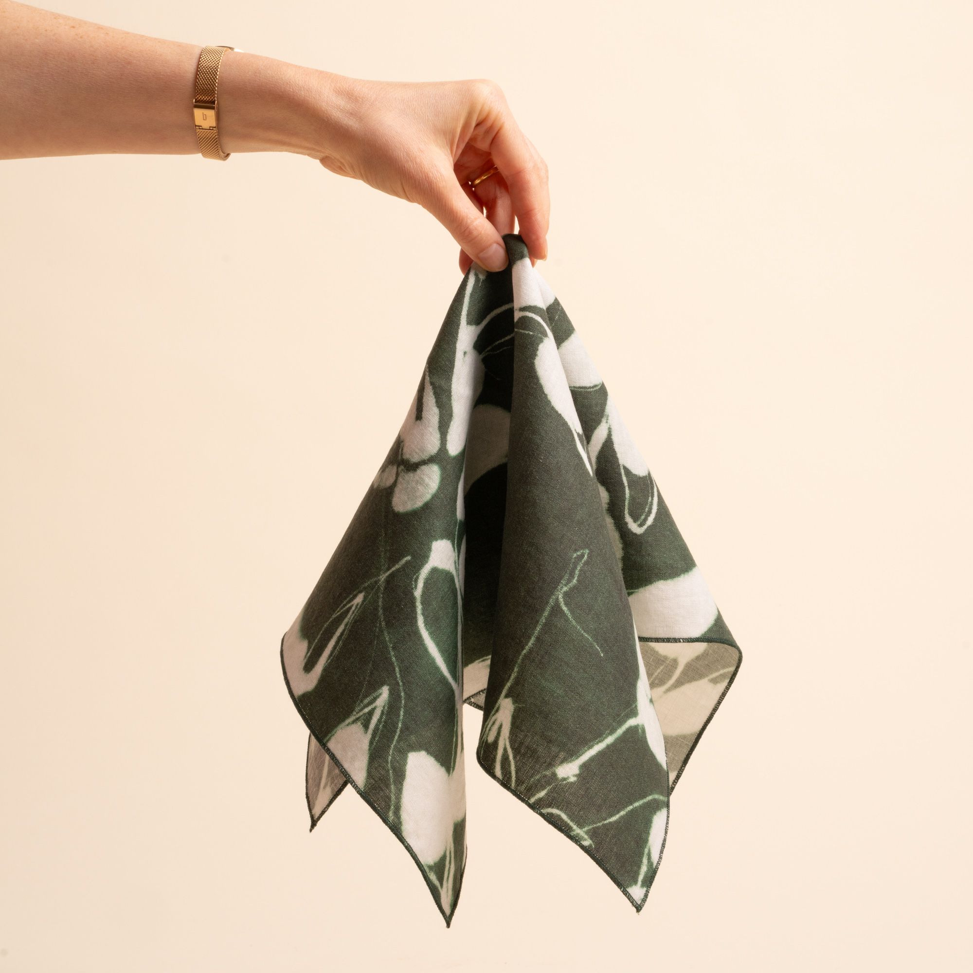 A hand holds out a dark green napkin with white botanical print on a neutral background.
