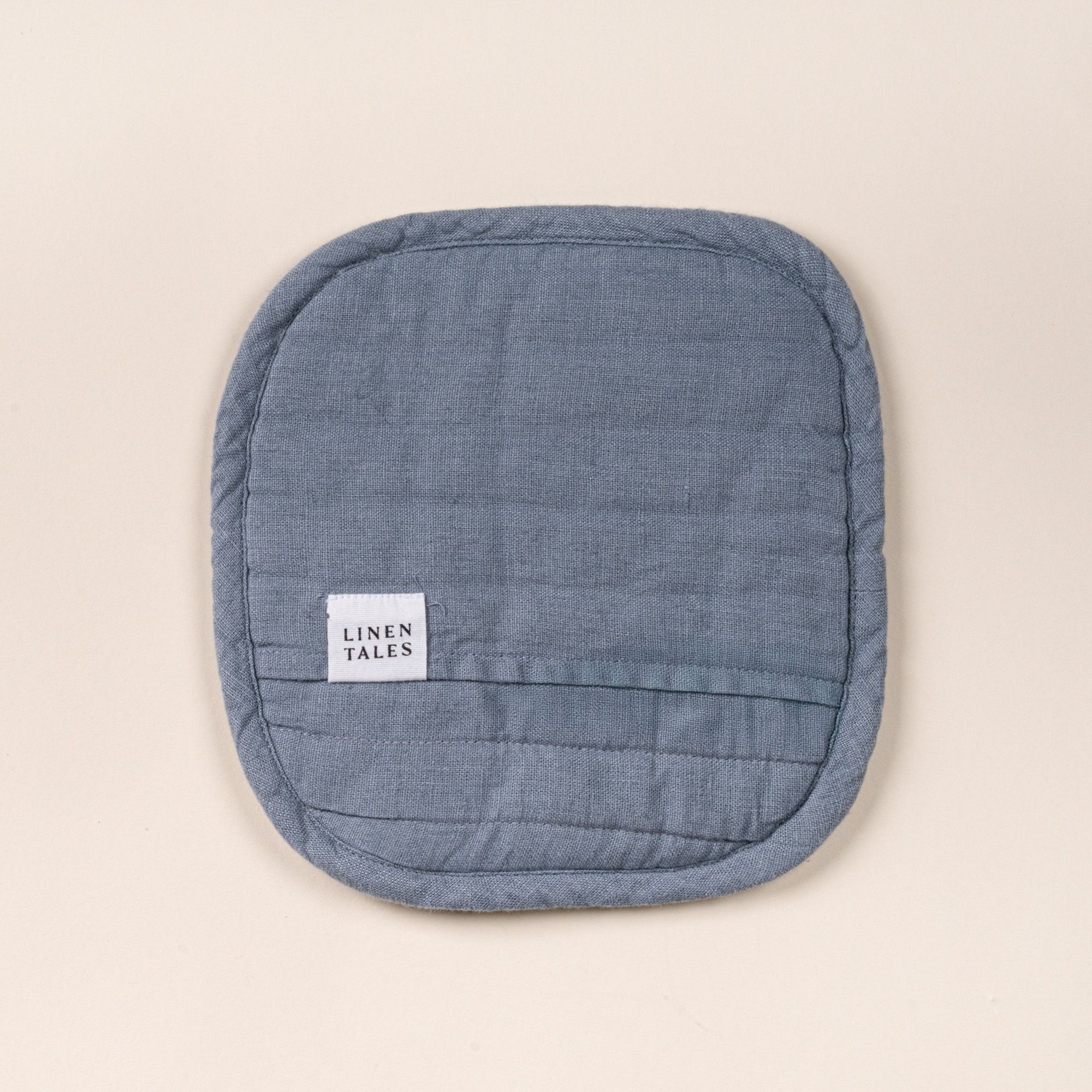 Square quilted linen potholder in a blue-grey color with rounded corners and a small ‘LINEN TALES’ label, on a light background.