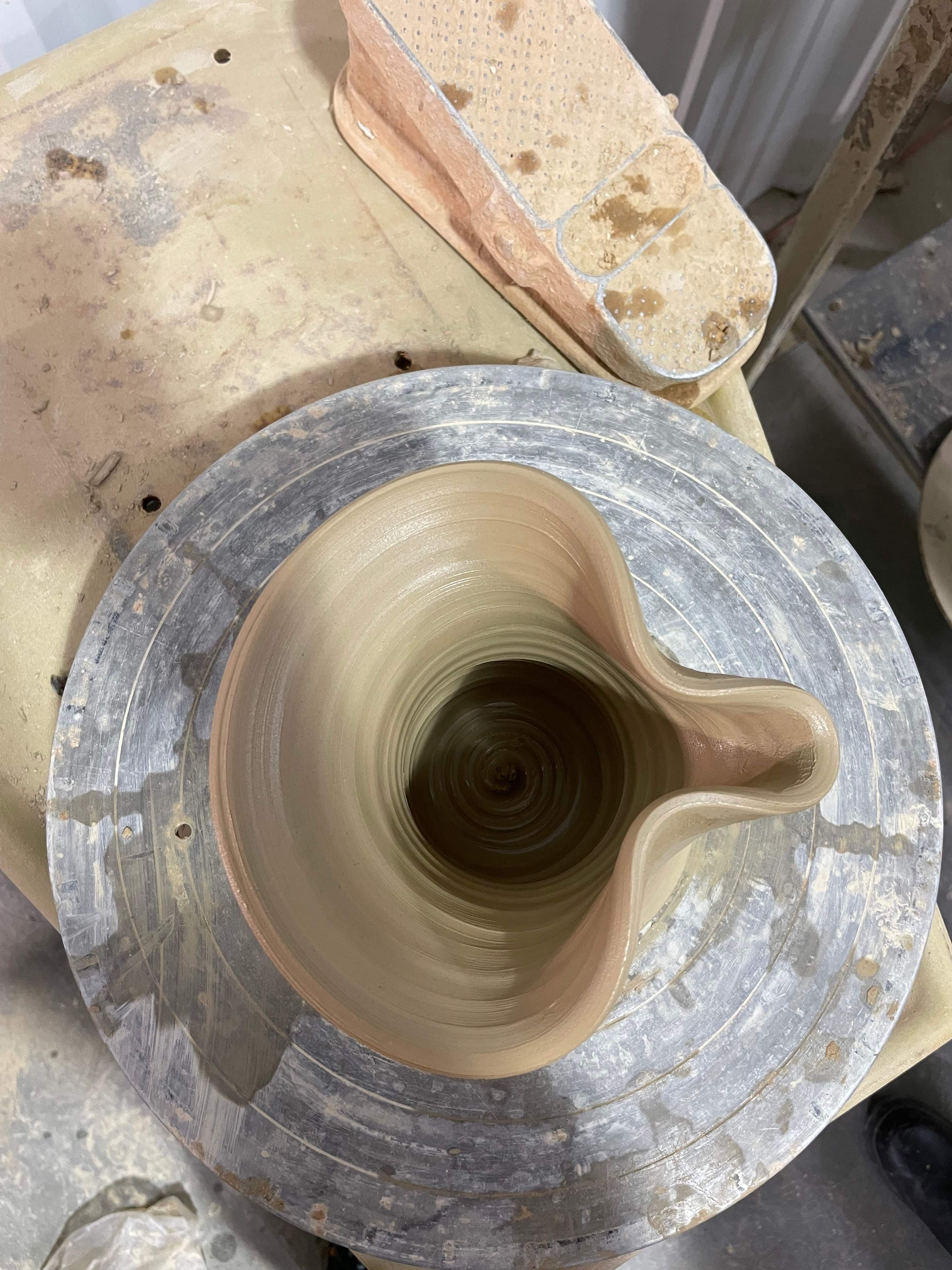 A hand thrown and shaped spout in clay on a potter's wheel