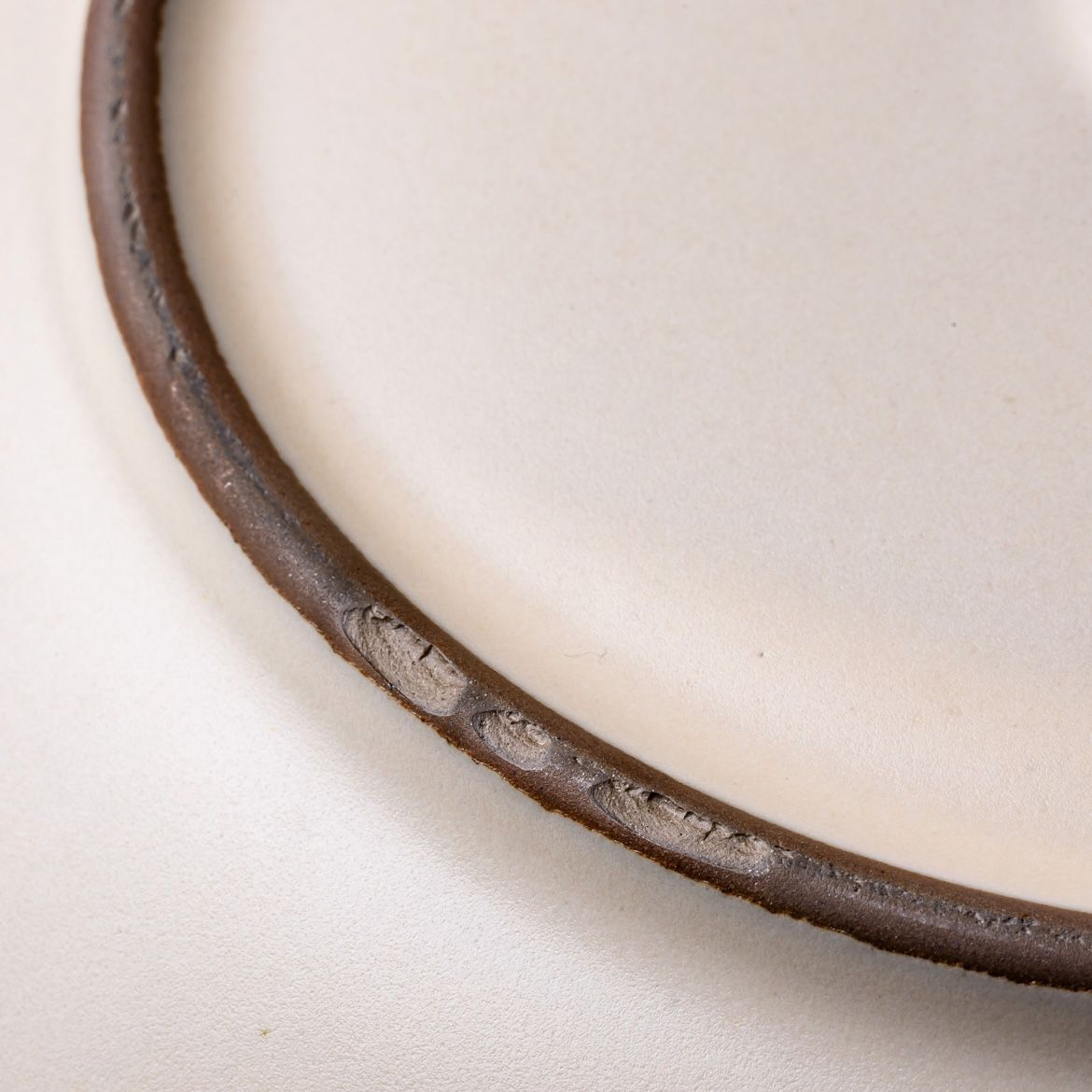 A closeup of an unglazed edge on a ceramic plate with scuffs.