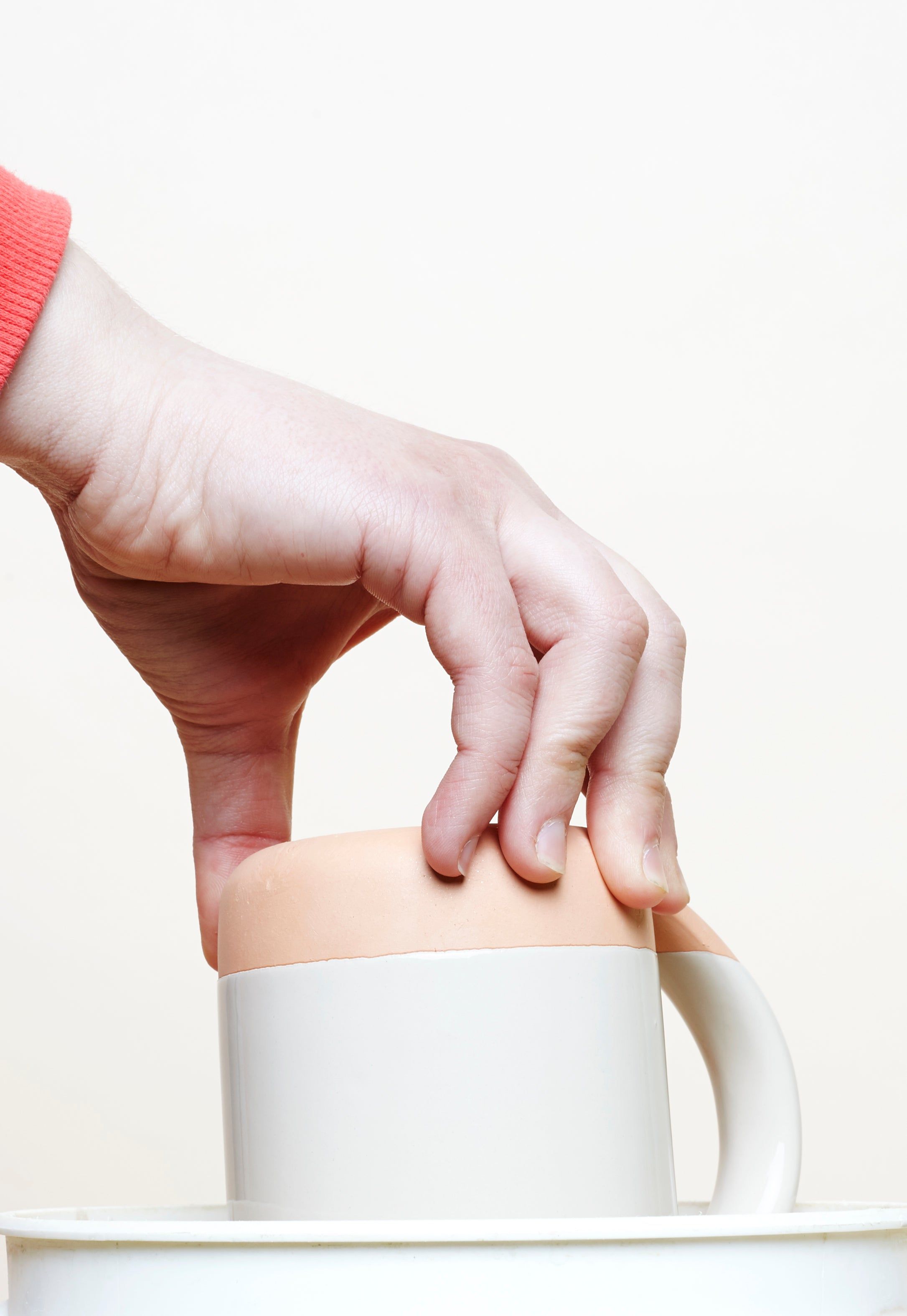 A hand holds the East Fork Mug upside down to dip it in a bucket of glaze