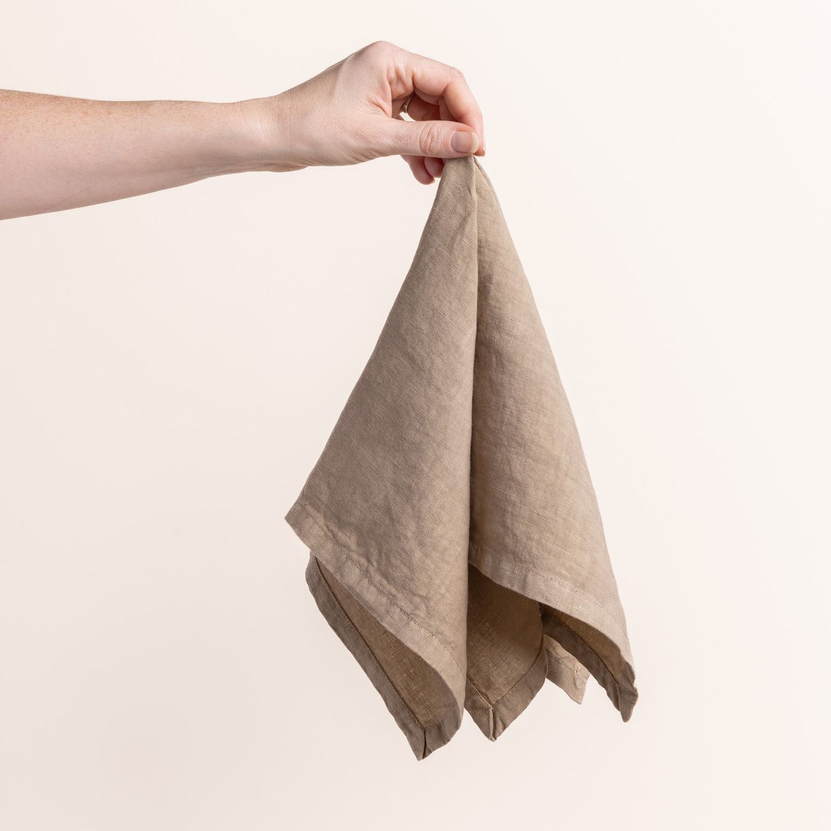 Hand holding a linen napkin in an soft warm brown color from the center 